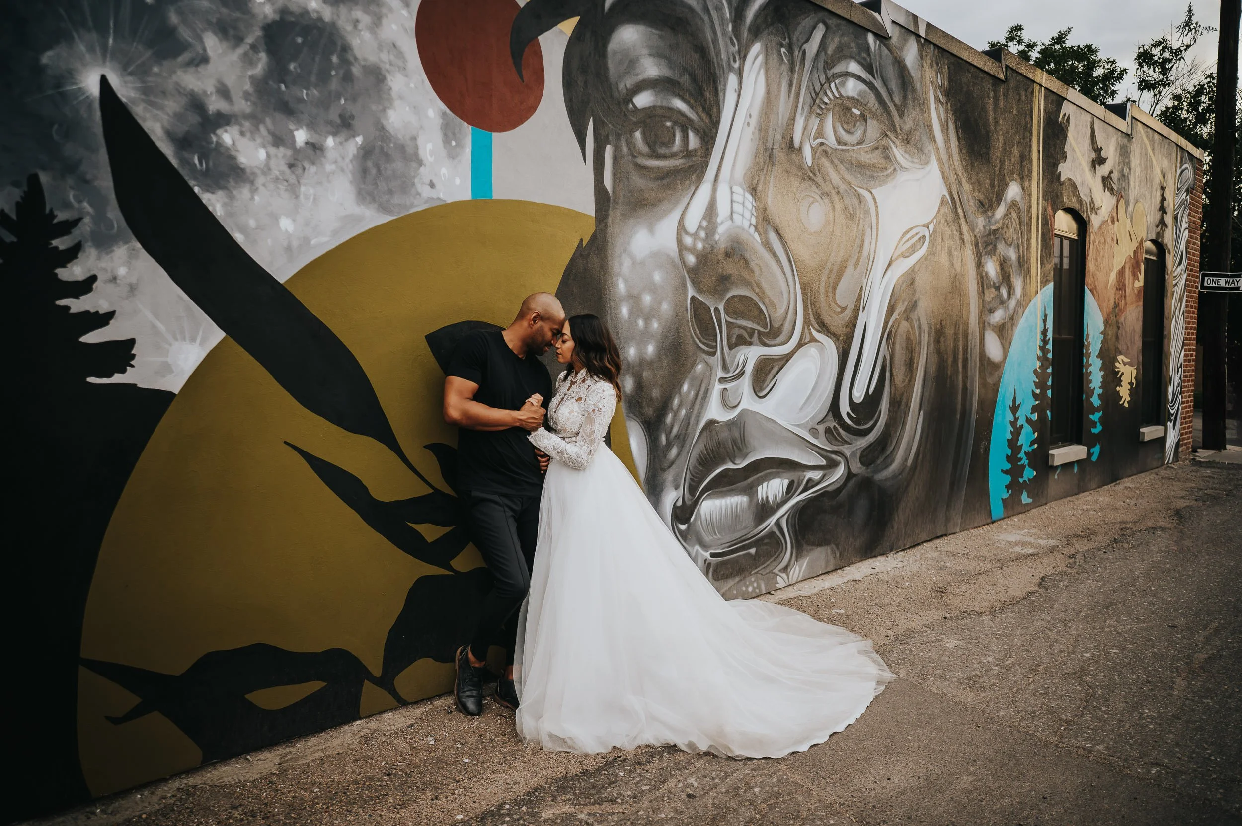 Bride and groom sharing a kiss in front of a large painted mural, bride in a full lace gown.