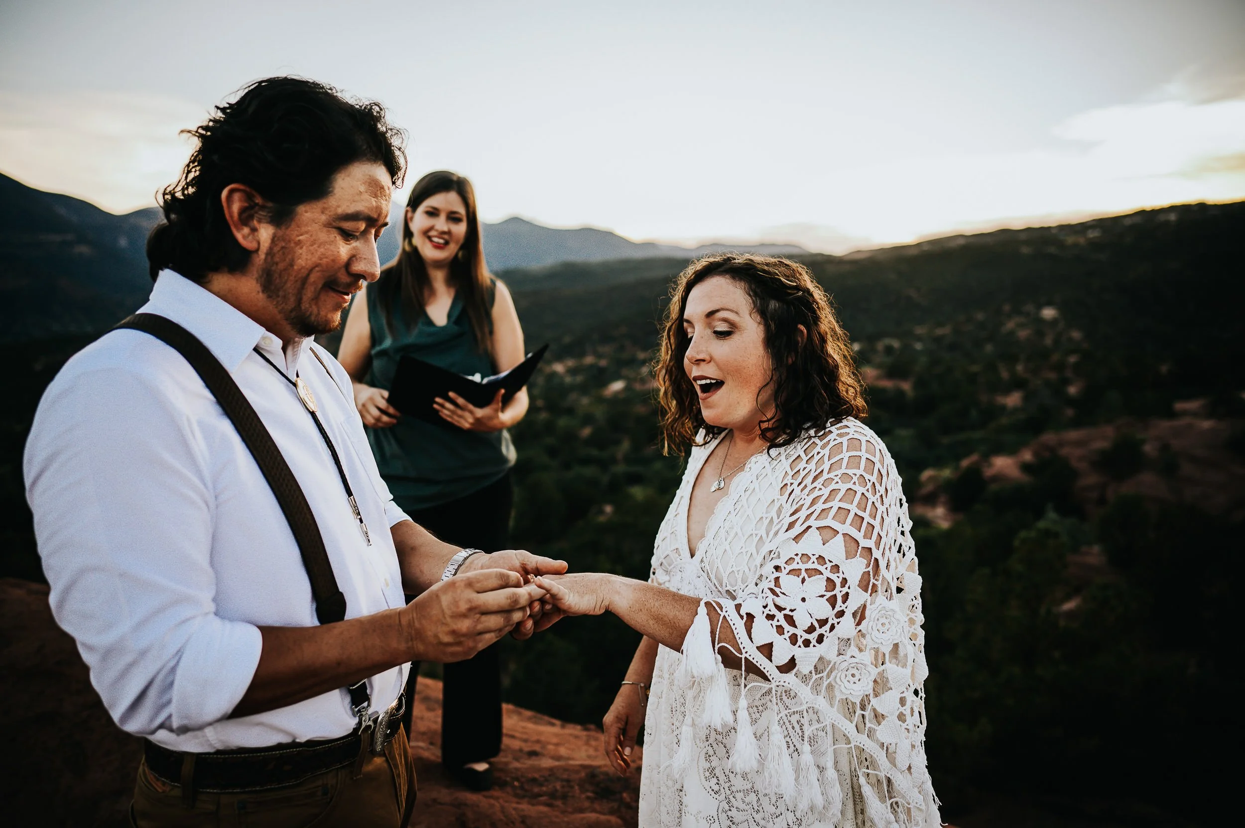 Couple exchanging rings during an outdoor elopement ceremony with mountains visible in the background.