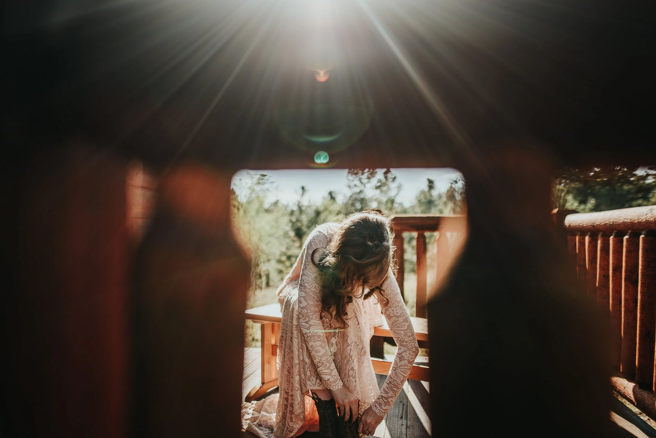 A bride adjusts something at a rustic wooden wheel, warm backlight pouring through, moody and atmospheric.