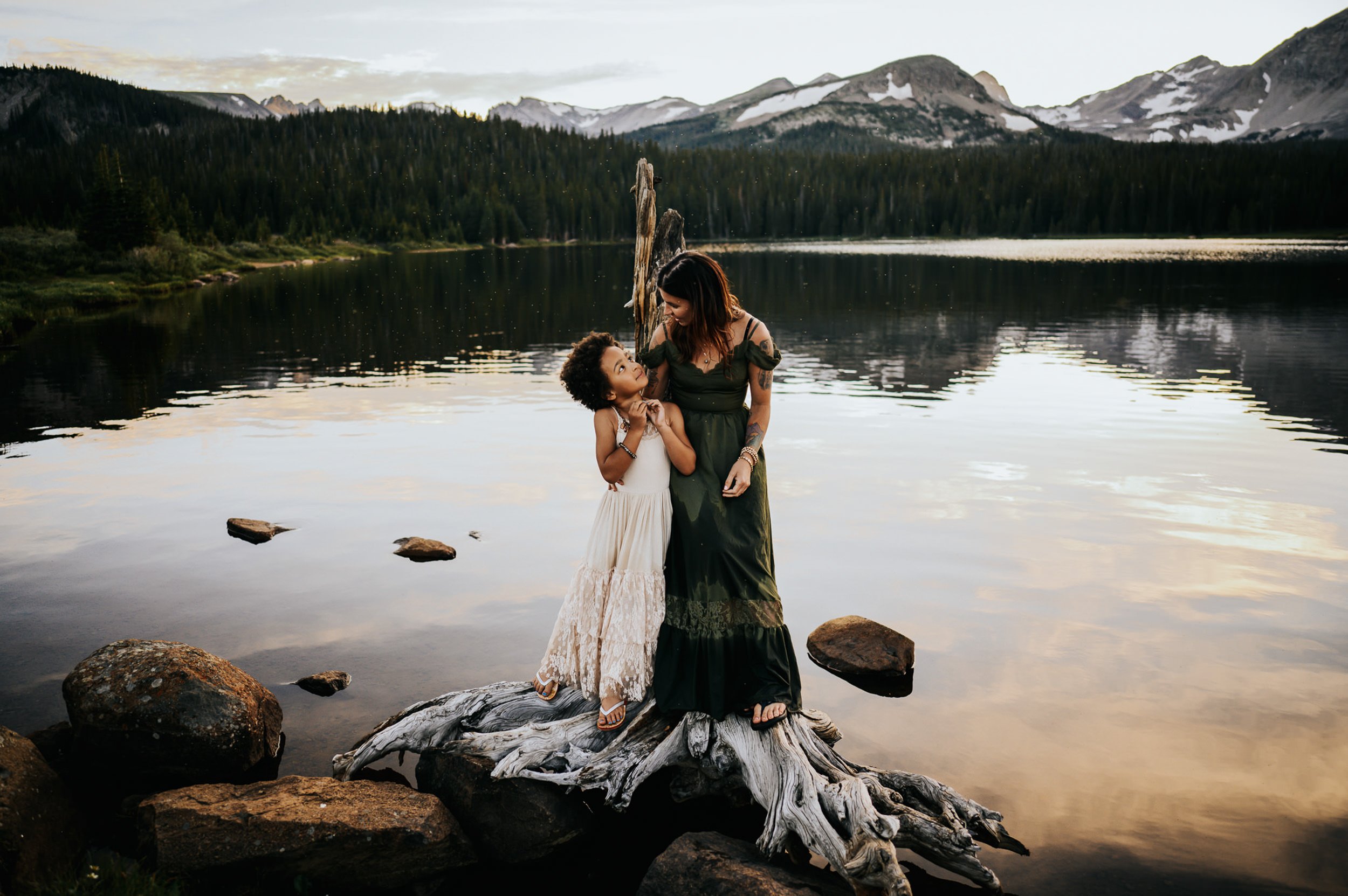 Family standing together at an alpine lake with mountains and evergreens behind them.