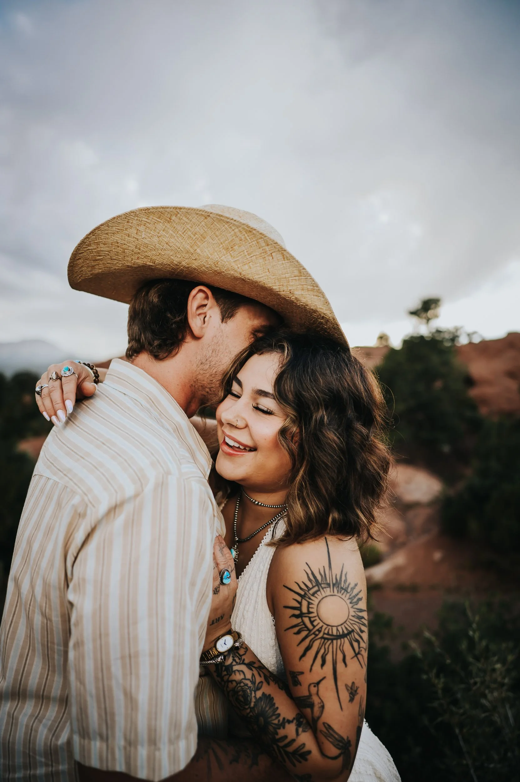 Intimate close-up of couple smiling together, both with visible tattoos, coordinated in cream and tan earth tones.