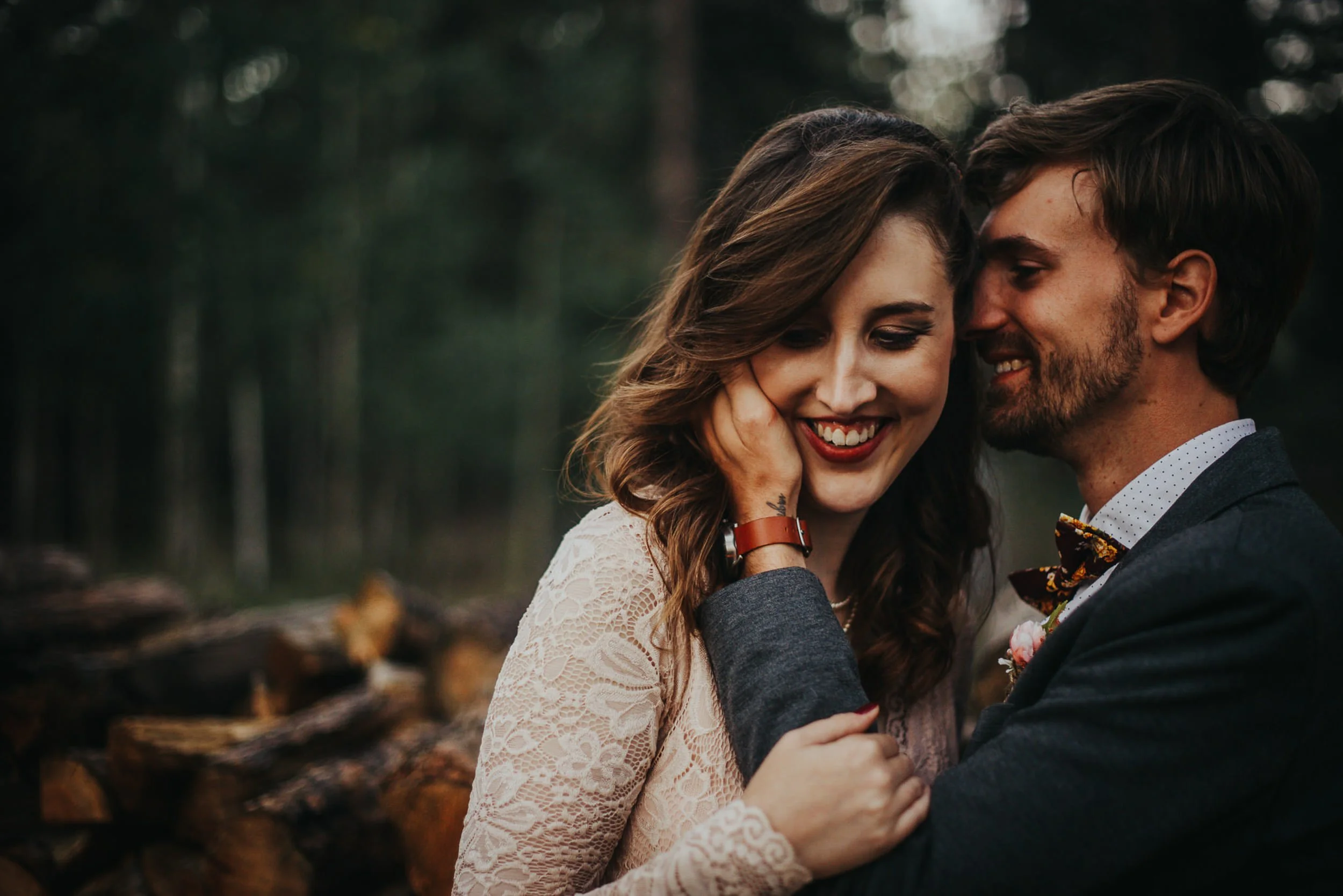 A groom nuzzles his bride's neck from behind, she laughs with red lips and rich curls.