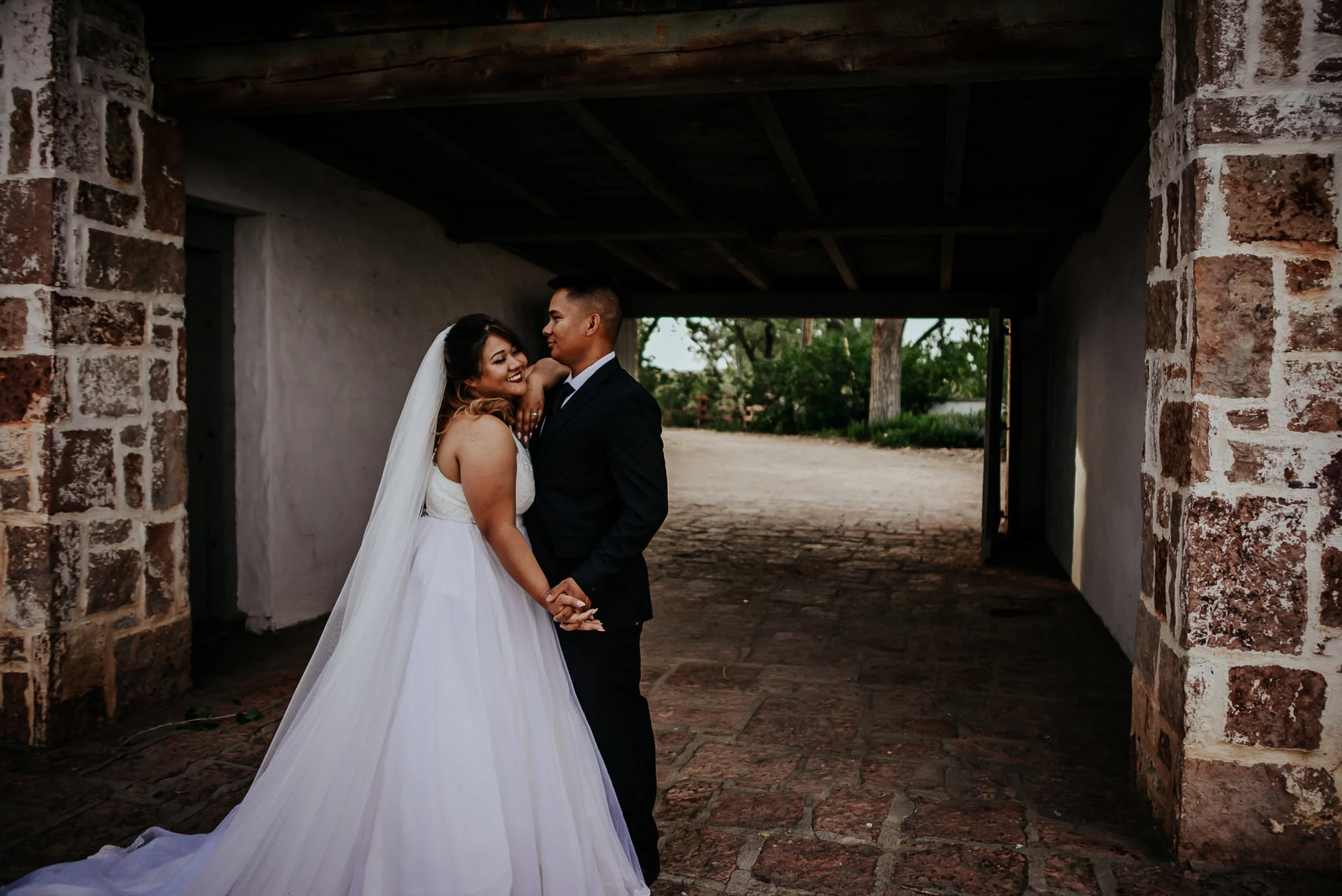 A bride and groom share a first look in a shadowed outdoor passageway, soft backlight.
