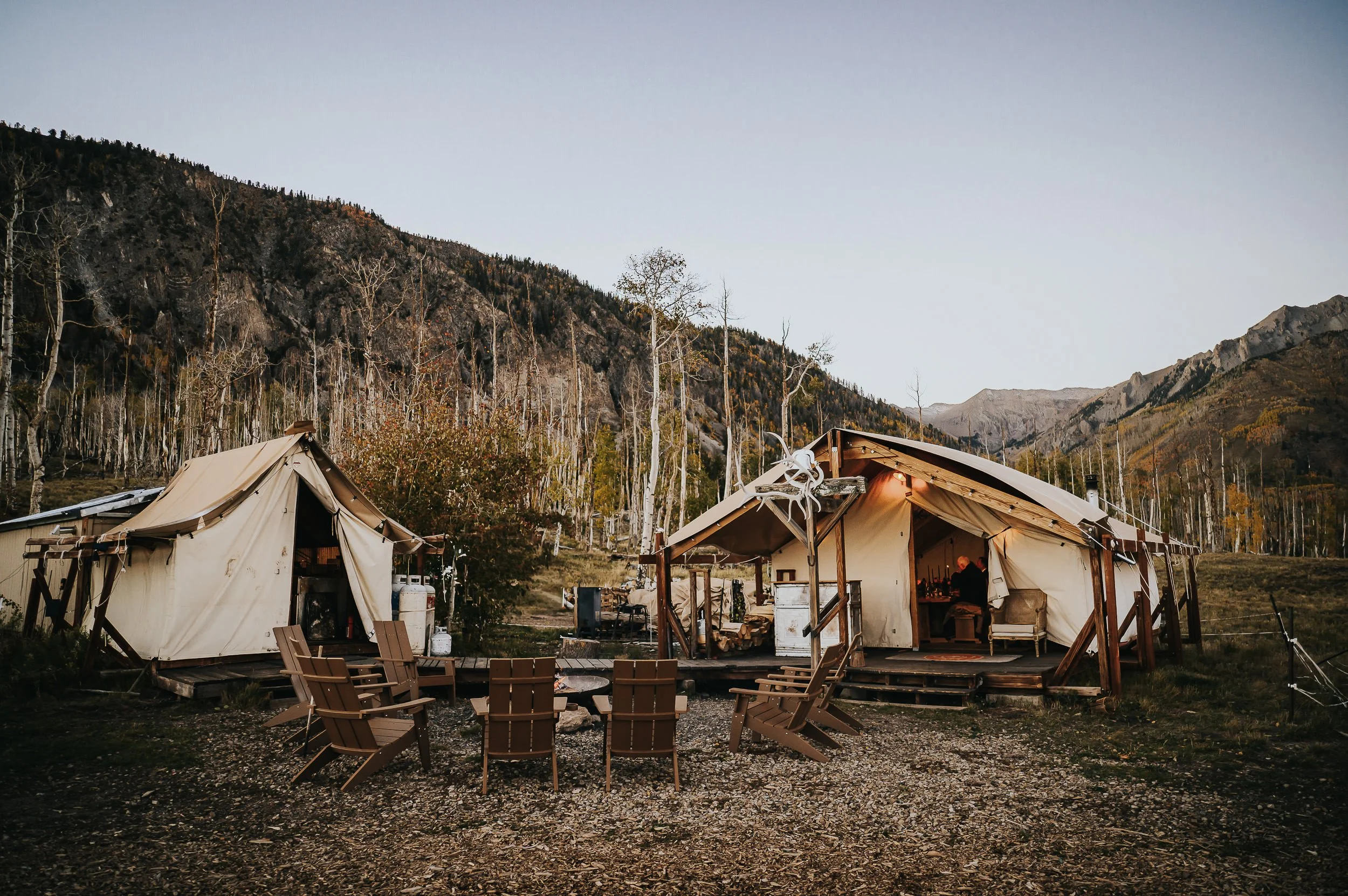 Canvas glamping tents set up in a golden aspen grove with mountain peaks in the background.