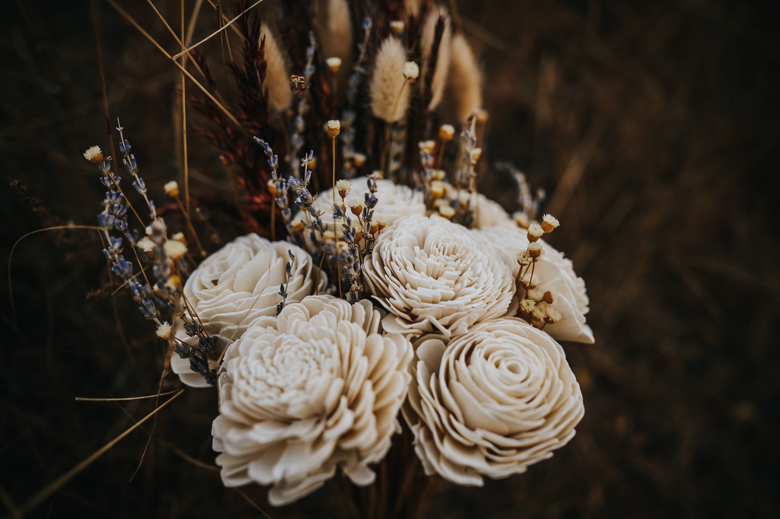 A dried floral bouquet flatlay with large cream blooms and soft textures on a dark surface.