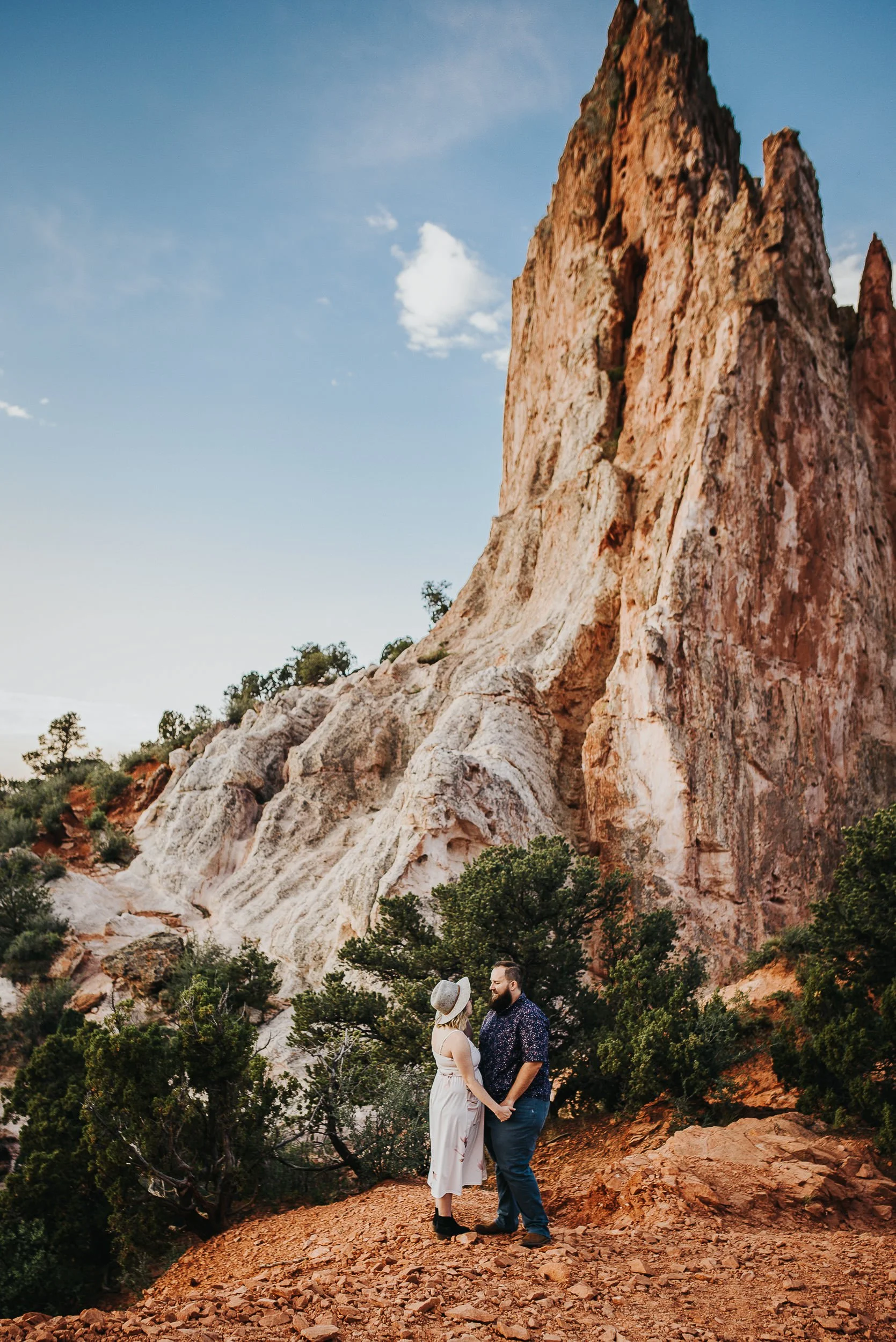 A bride's long lace train cascades down boulders at Garden of the Gods, wide dramatic landscape shot.