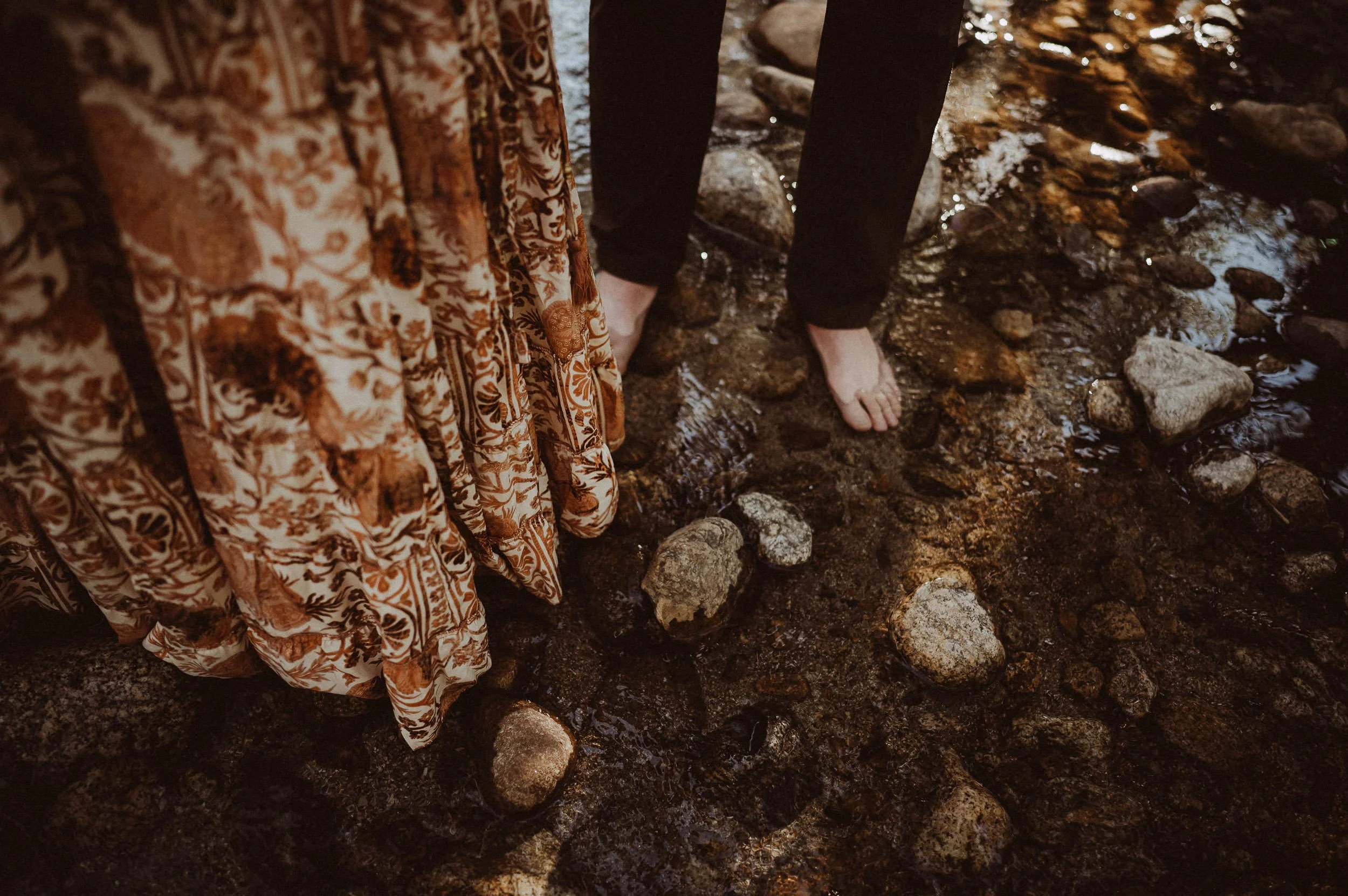 Close crop of a bride's lace dress hem standing at the edge of water at Field of Vision.