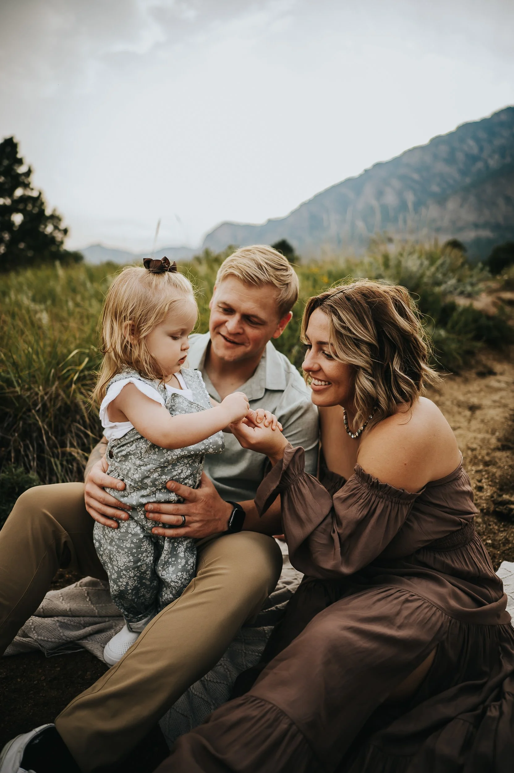 A family sits together in a grassy Colorado foothills meadow, warm and relaxed.