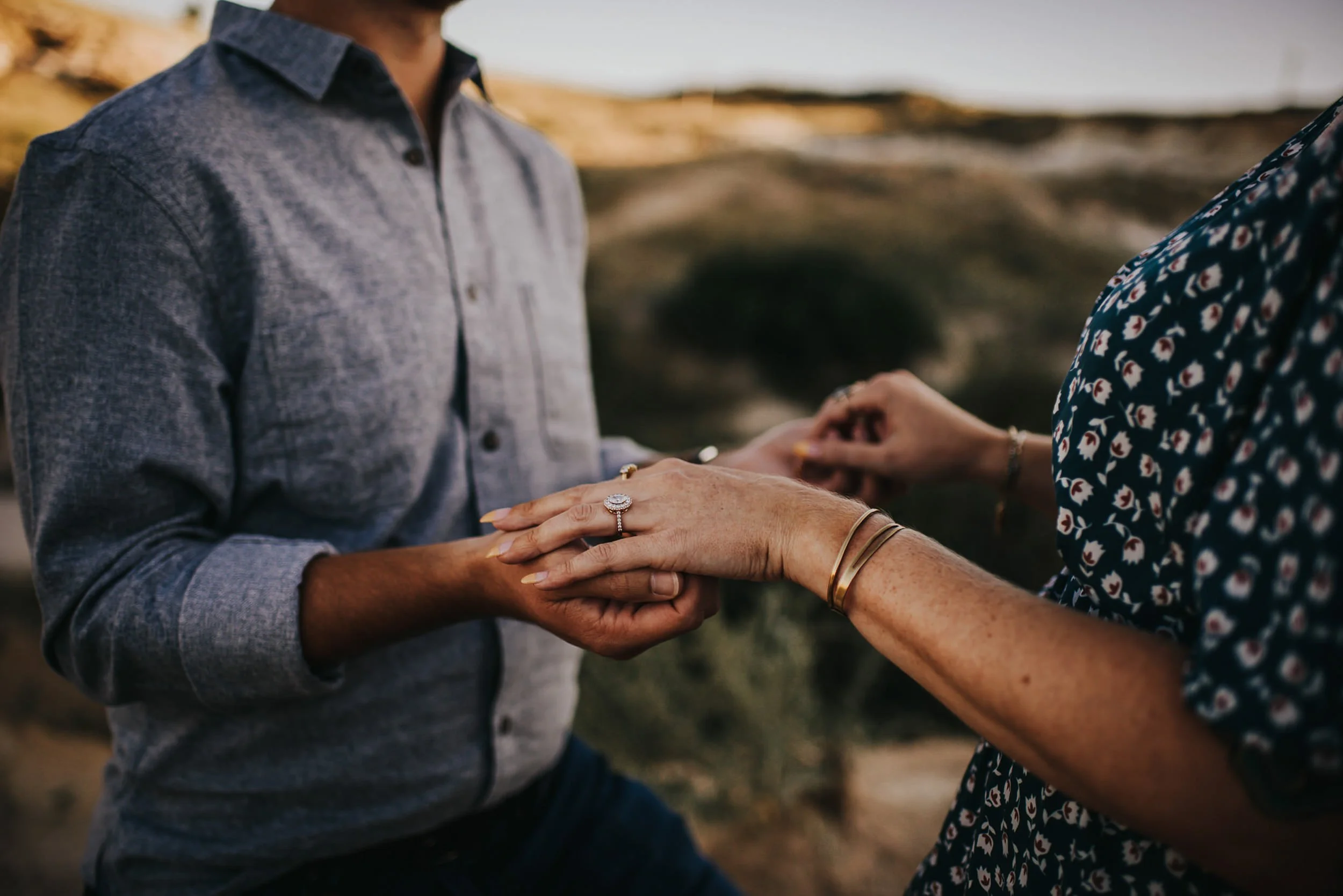 A closeup of a man sliding a ring onto his partner's finger, her floral dress visible, tender ceremony moment.