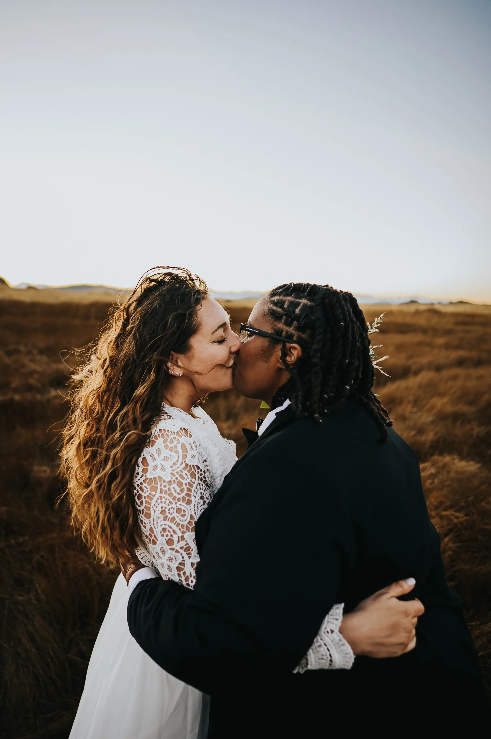 Golden light wrapping around two brides as they exchange rings in a mountain meadow.
