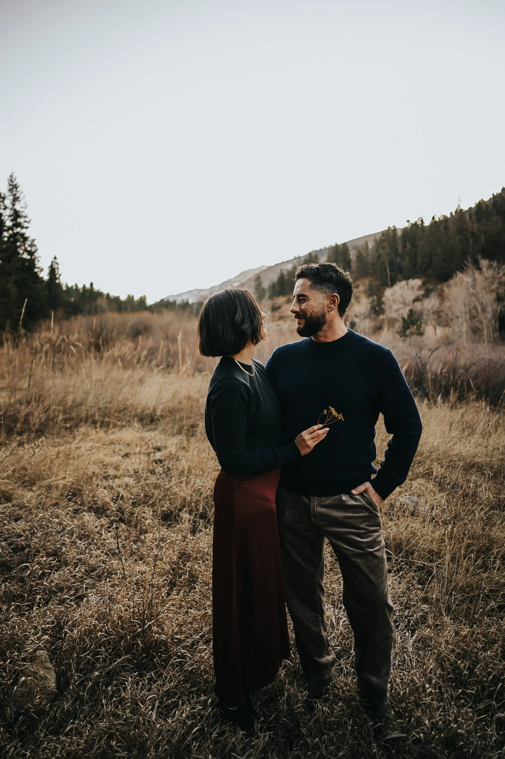 A couple stands together in a Colorado autumn landscape, she in burgundy, quiet and connected.