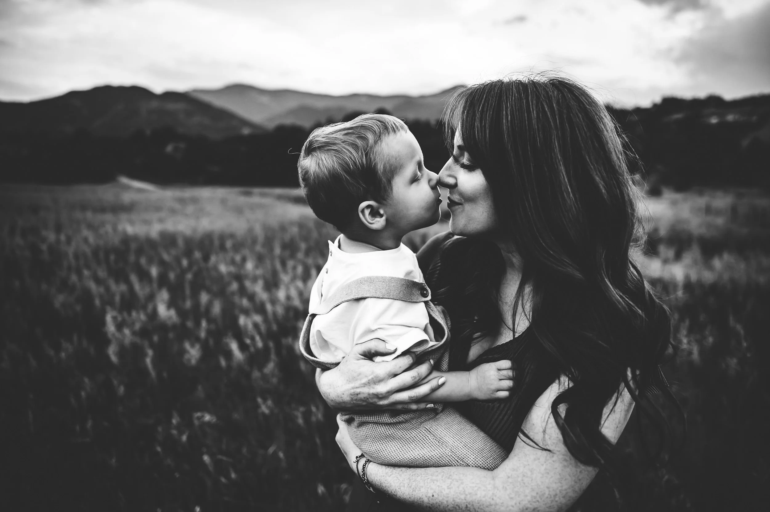A mother gives her son nose kisses in a field with mountains behind at Red Rock Canyon Open Space in Colorado Springs.