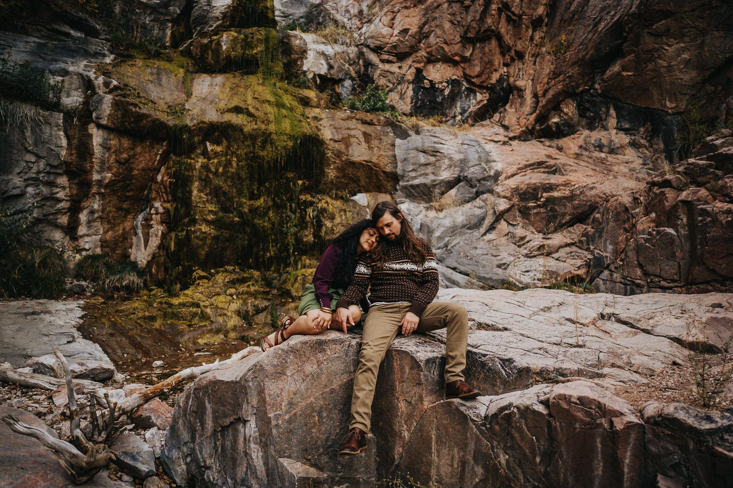 A couple sits together on boulders in a dramatic rocky canyon, adventurous and close in Williams Cayon, Manitou Springs.