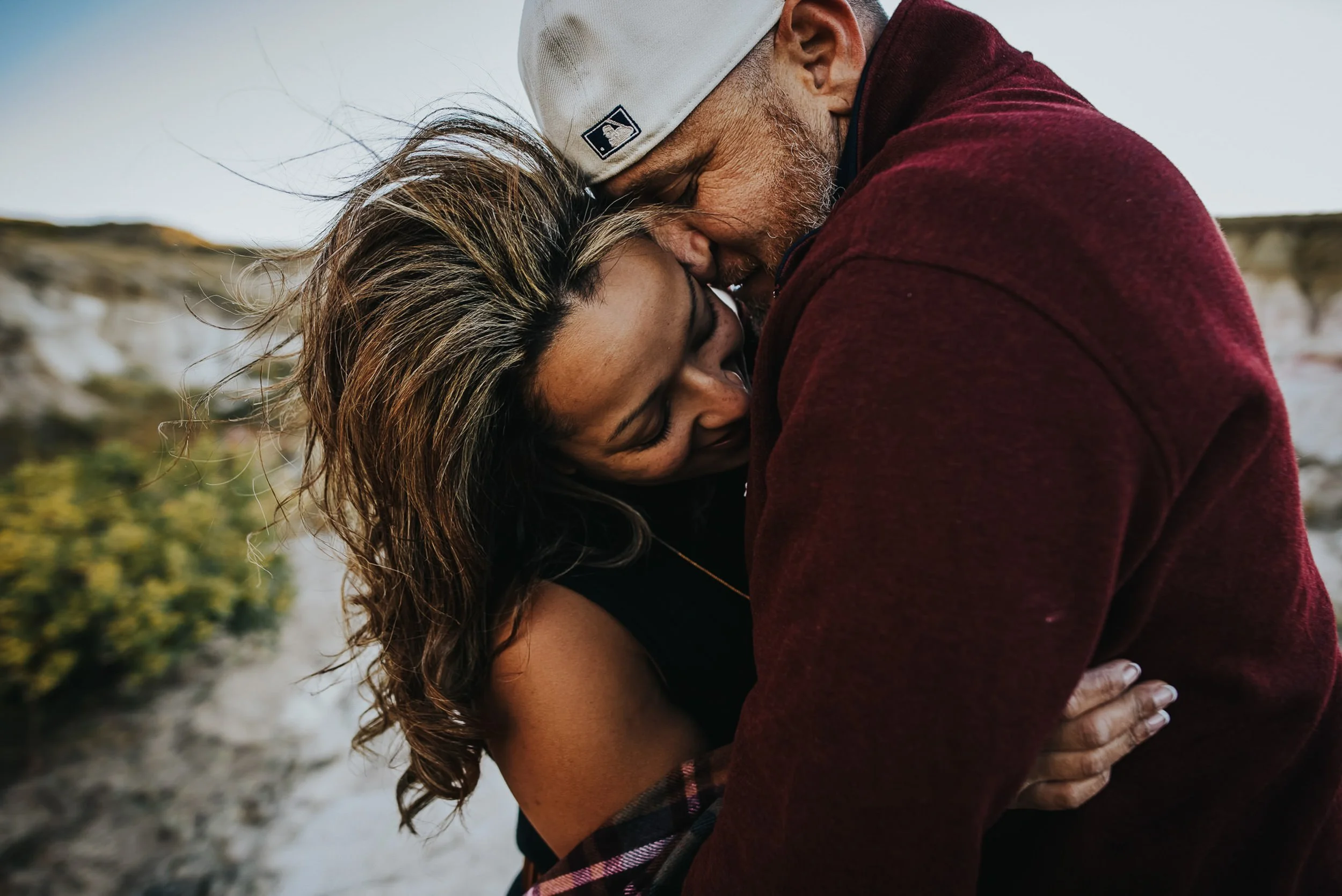 A man kisses his partner on the temple from behind, she smiles with her eyes closed, intimate closeup at the Paint Mines.