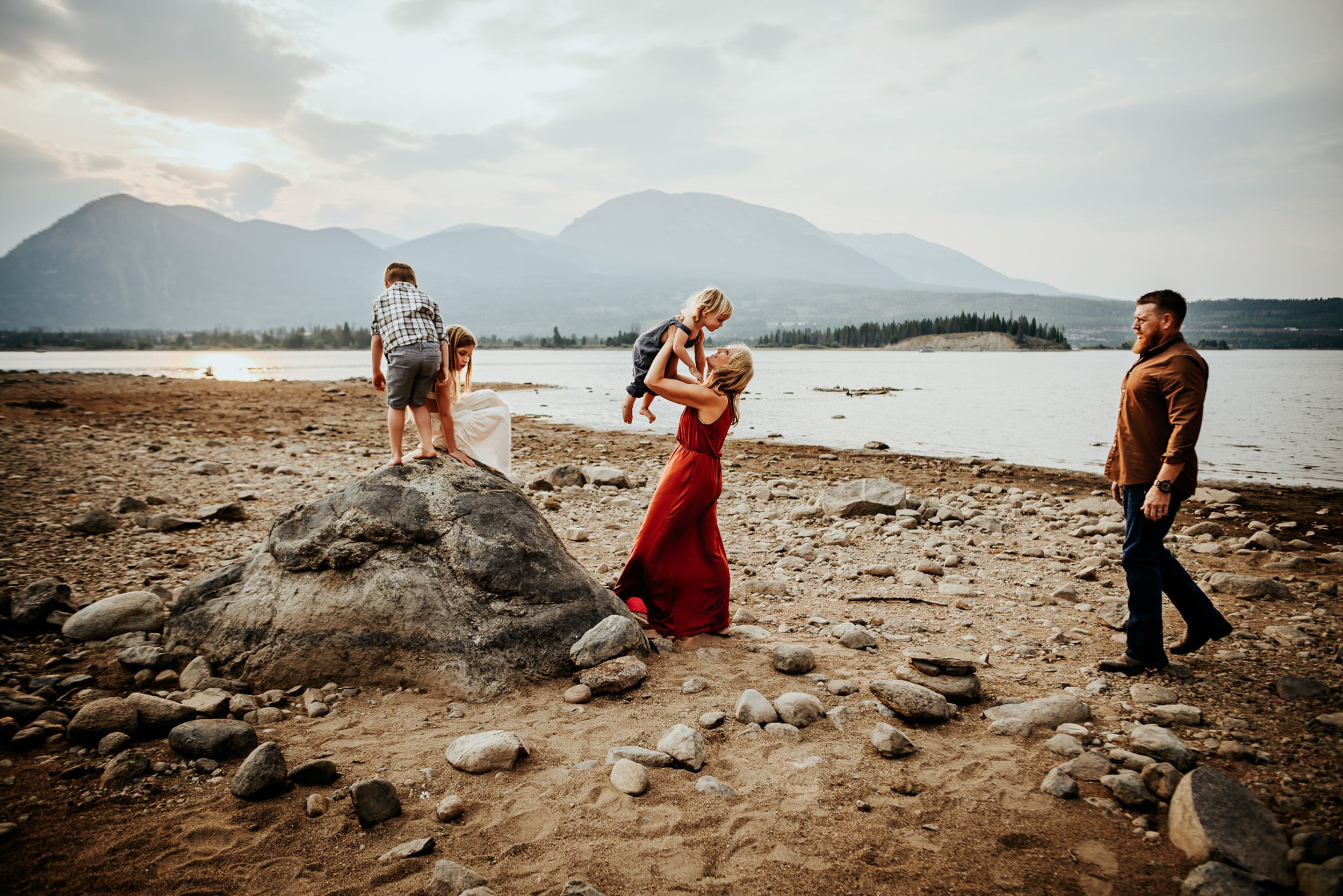 Family playing at the water's edge at Lake Dillon with mountains and golden sunset light.