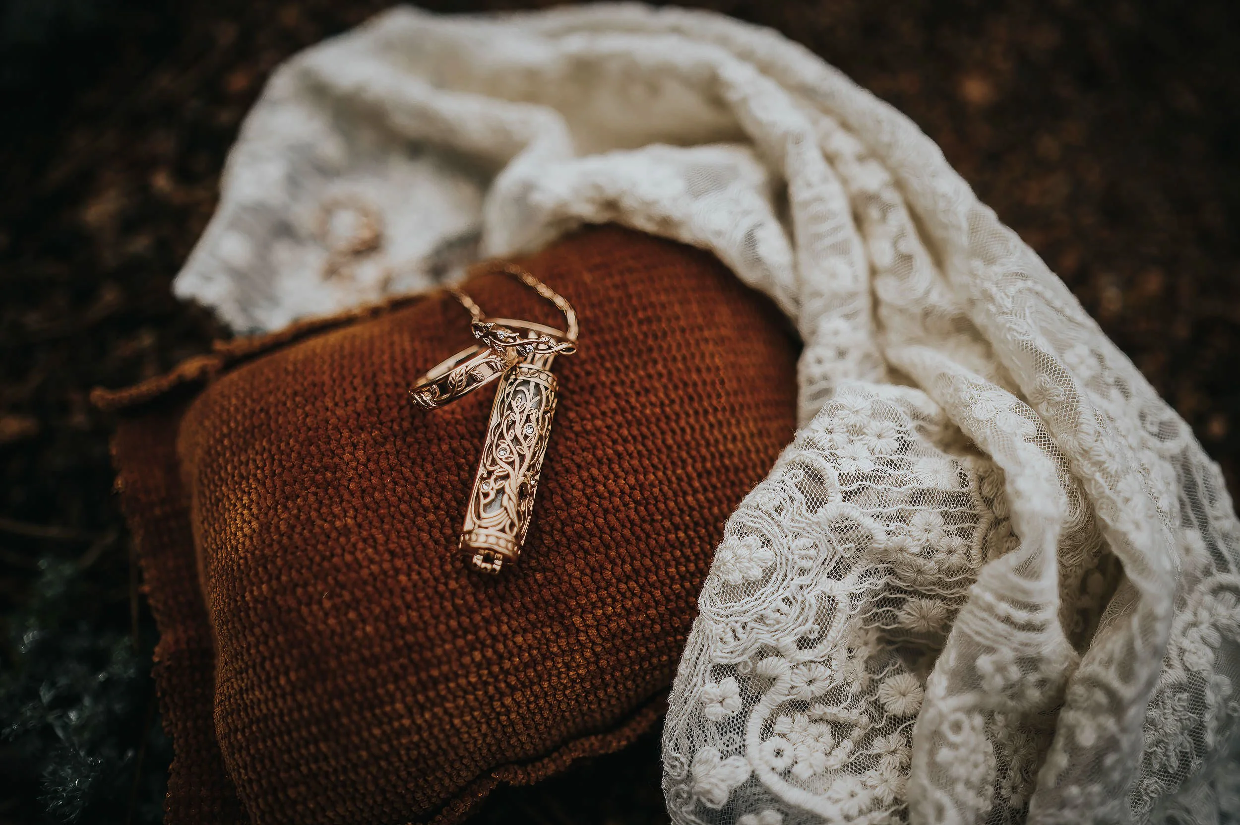 A wedding ring rests on a rust-colored knit fabric alongside a lace veil, soft detail flatlay.