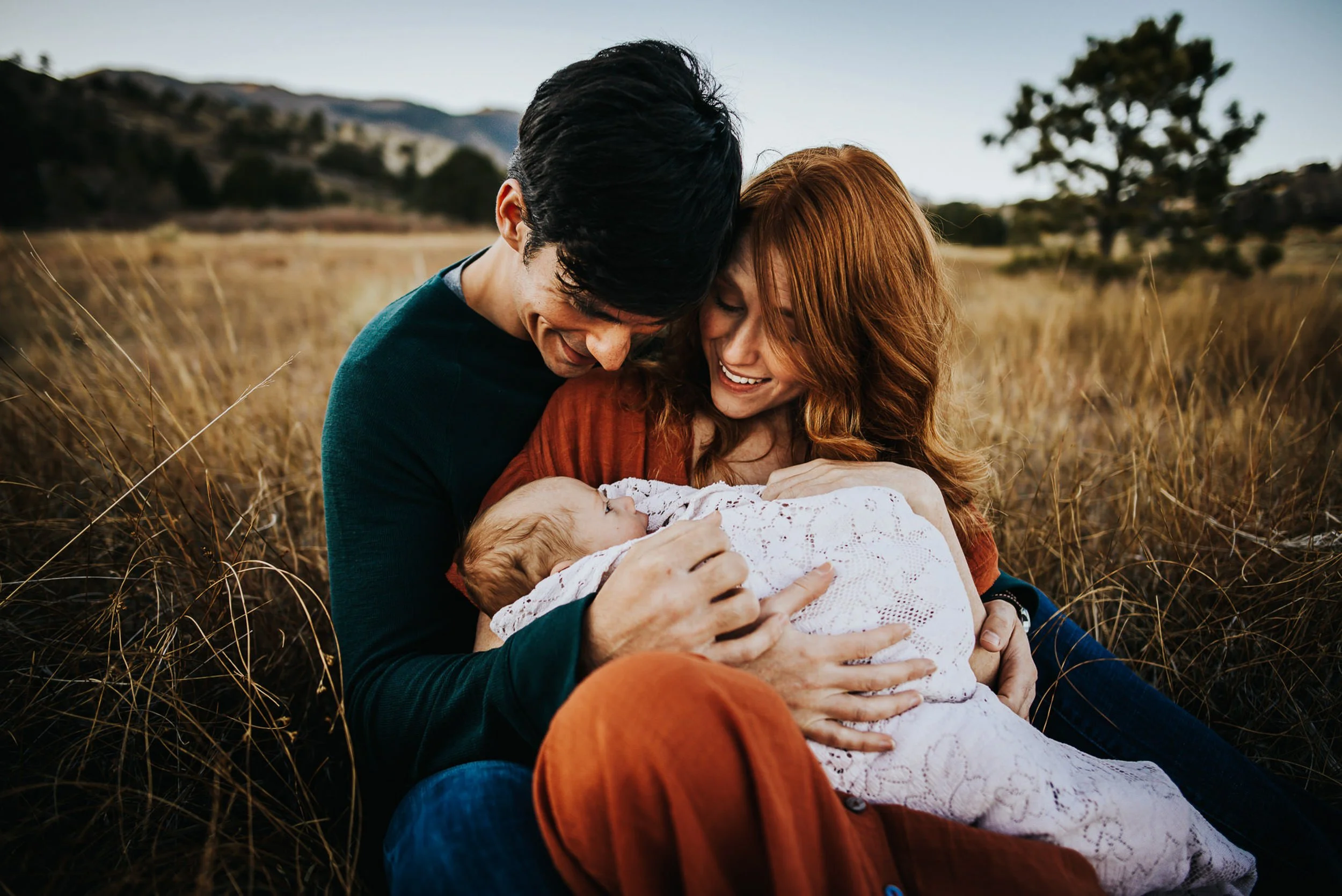 Parents cradling newborn baby in coordinated rust and neutral tones during intimate newborn family session.