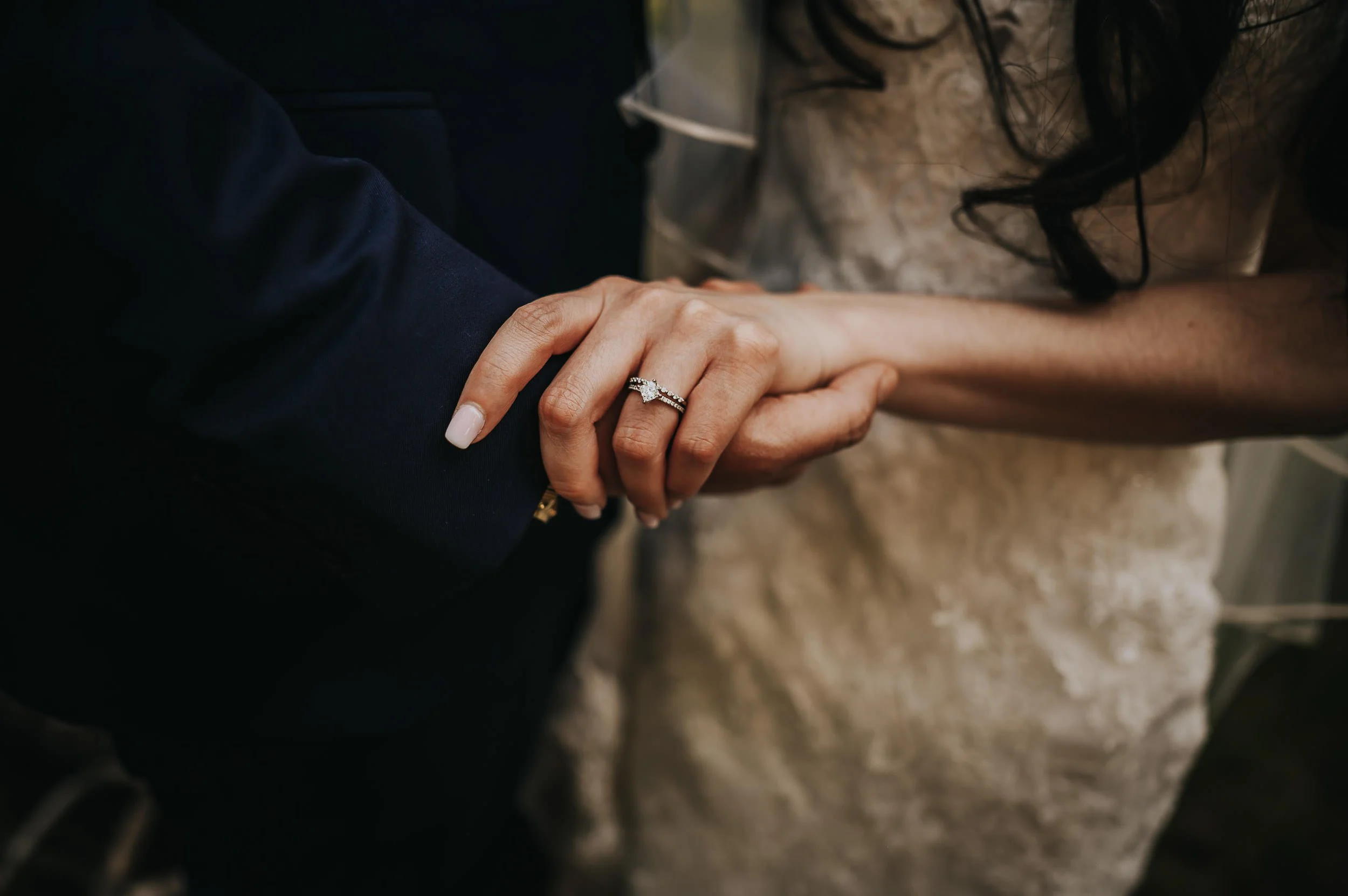 A closeup of a woman's hand with an engagement ring, his hand cupped gently beneath hers.