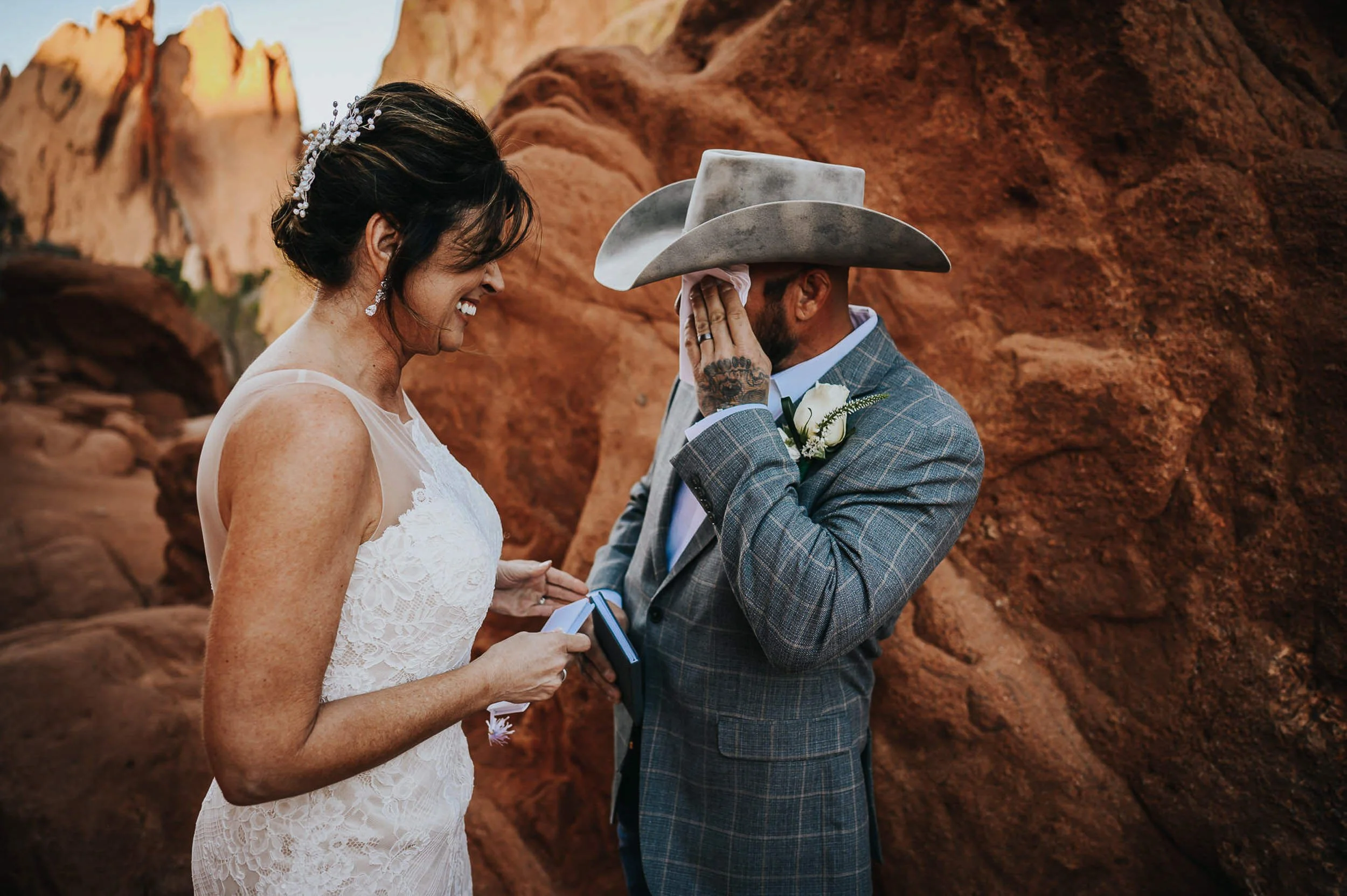 A bride in a full gown and groom in a suit exchange vows at Garden of the Gods, red rocks behind them.