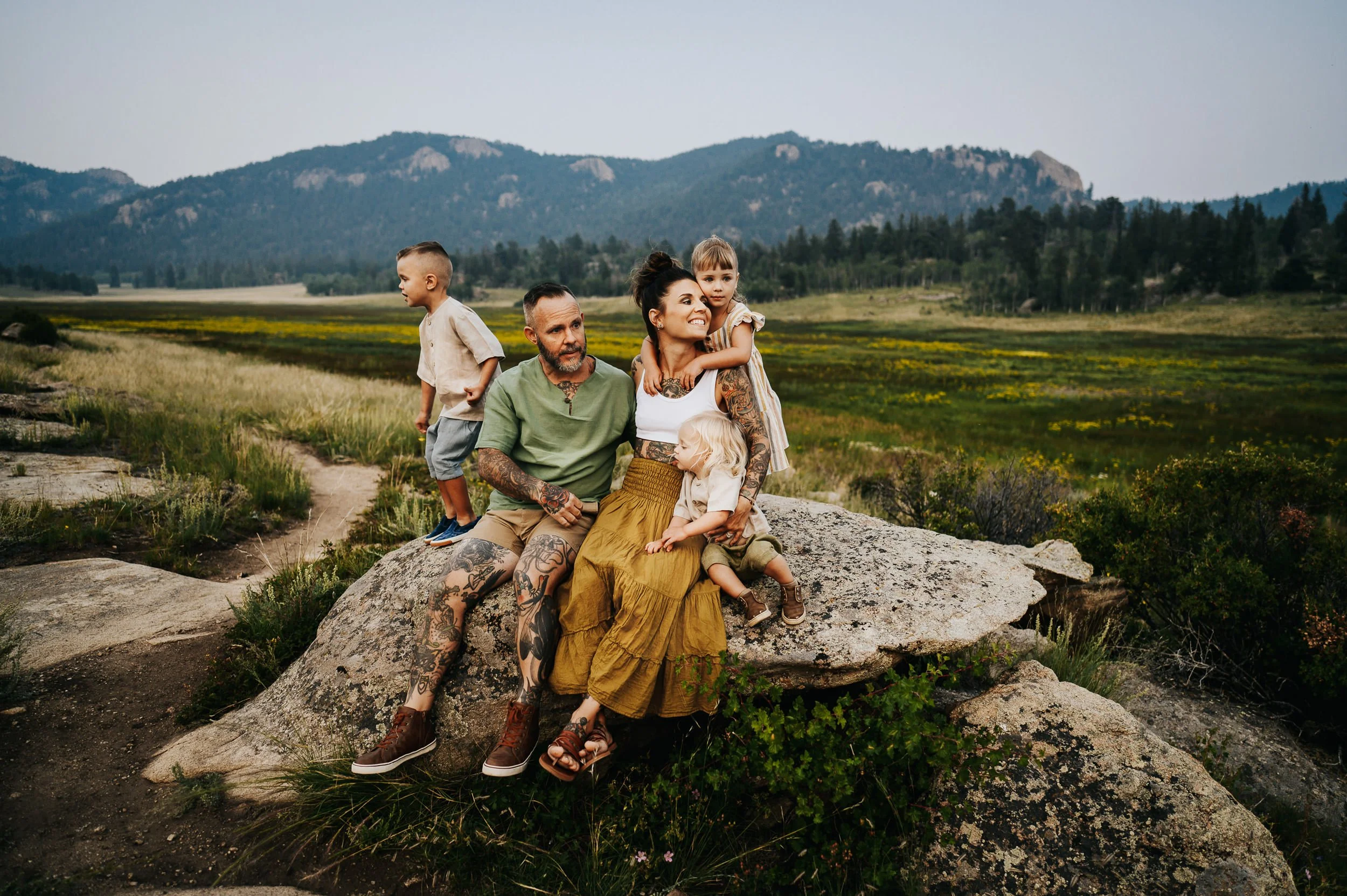 Family of four sitting together on boulders with Colorado mountain views behind them.