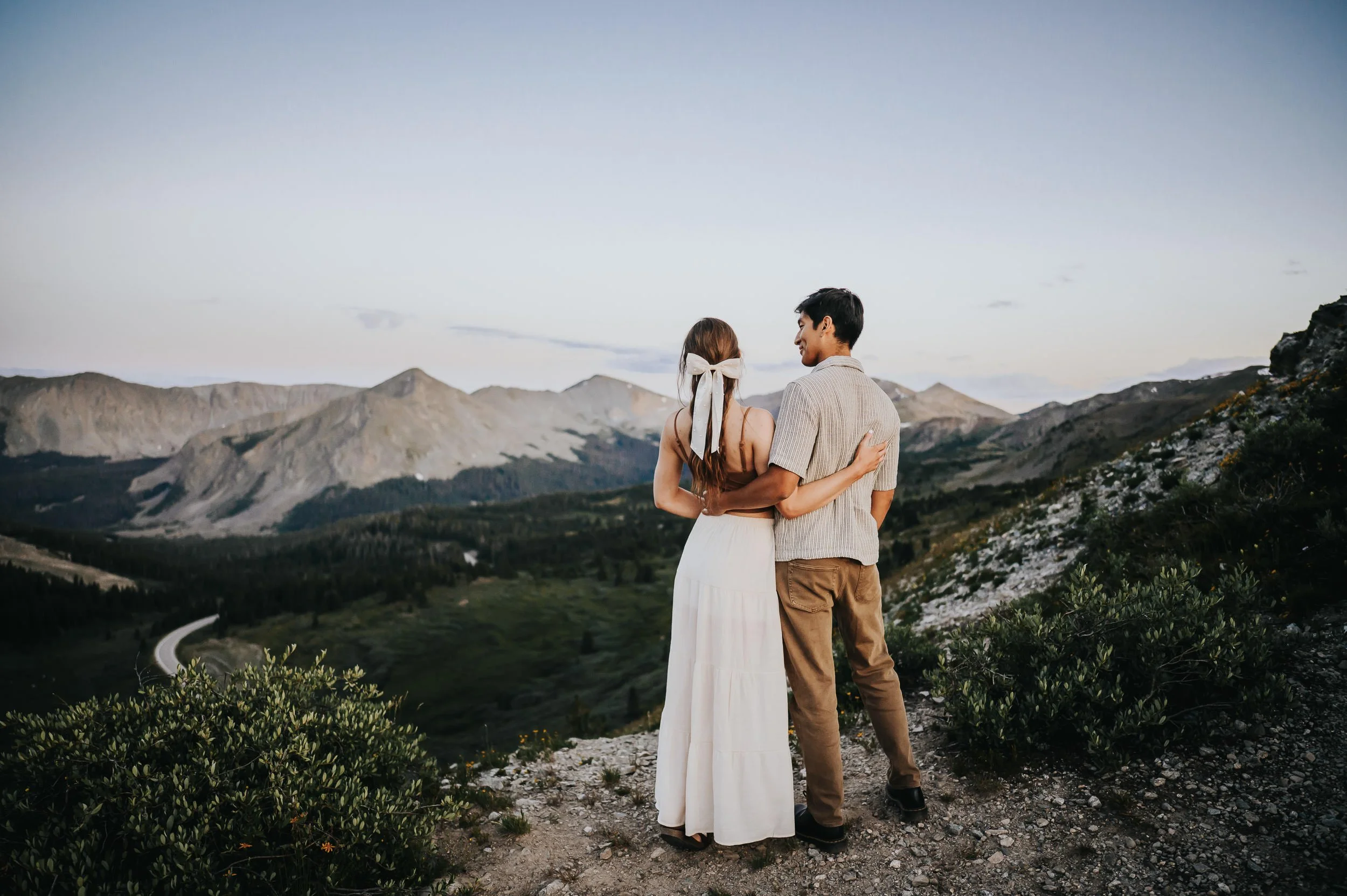 Couple walking hand in hand through a mountain meadow with Colorado peaks behind them.