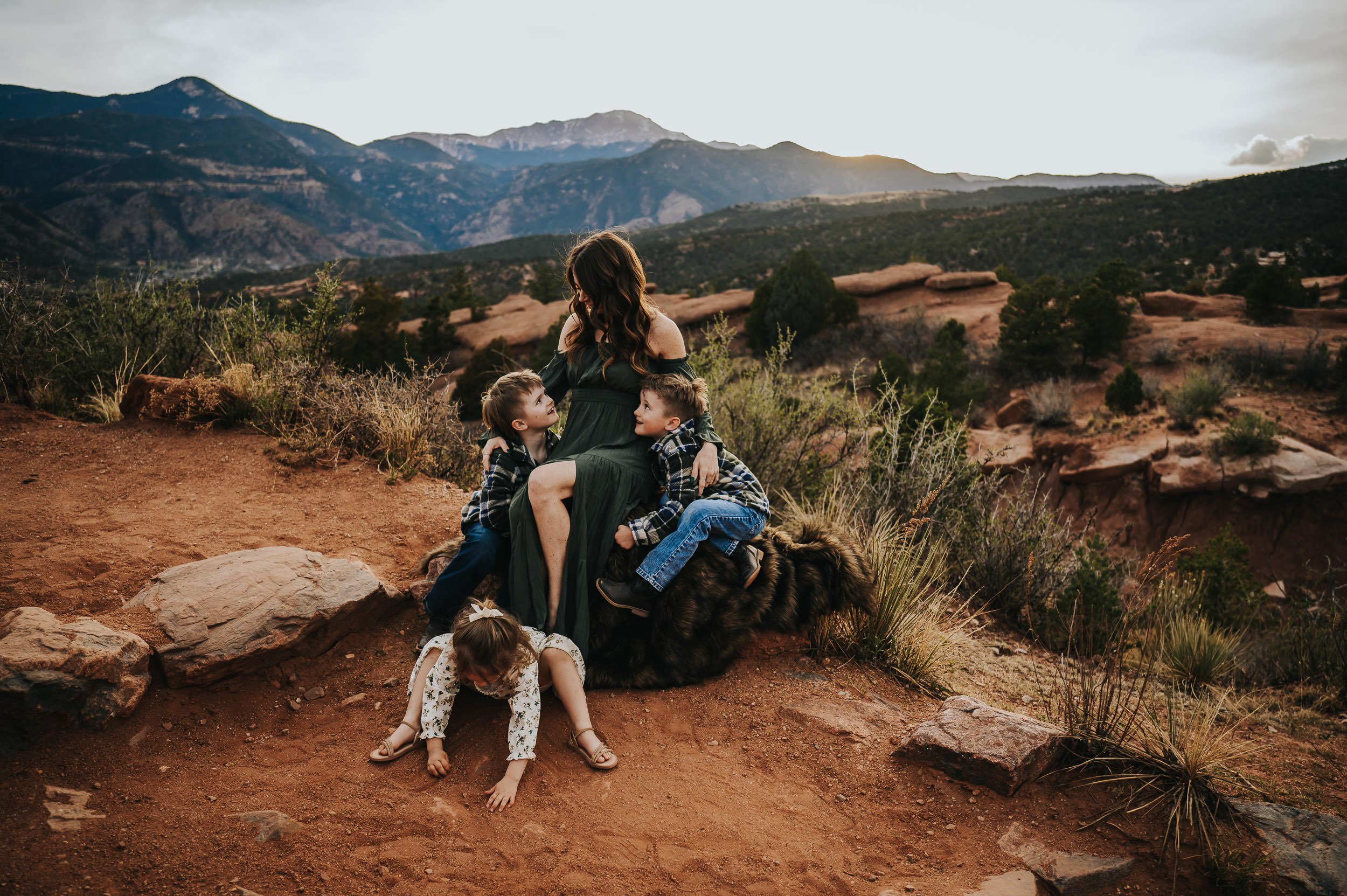 Mom sitting on red rocks with her three children gathered close, warm evening light at Garden of the Gods.