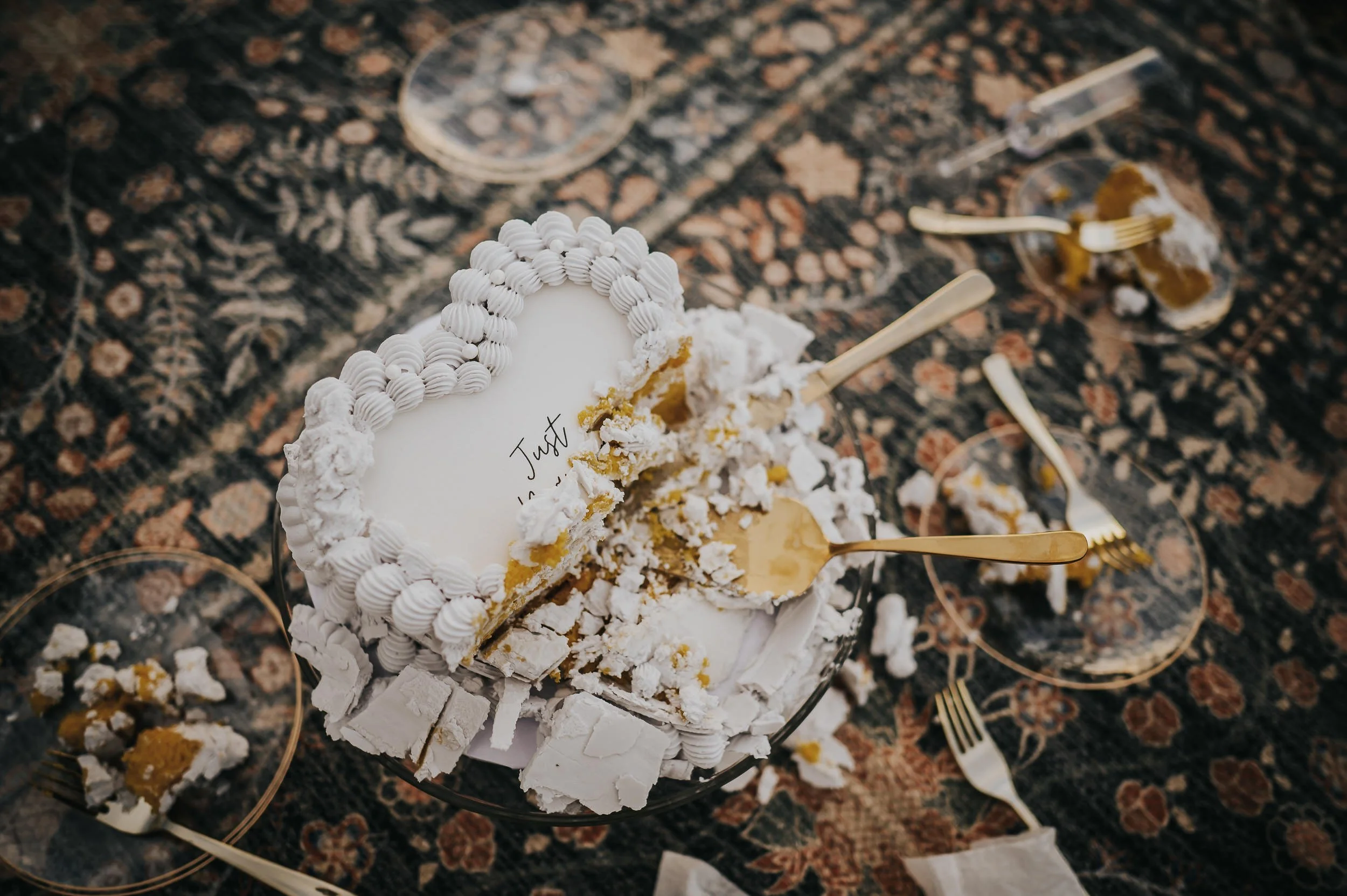 Overhead view of a white wedding cake with gold leaf details, crystals, and florals on a decorative surface.