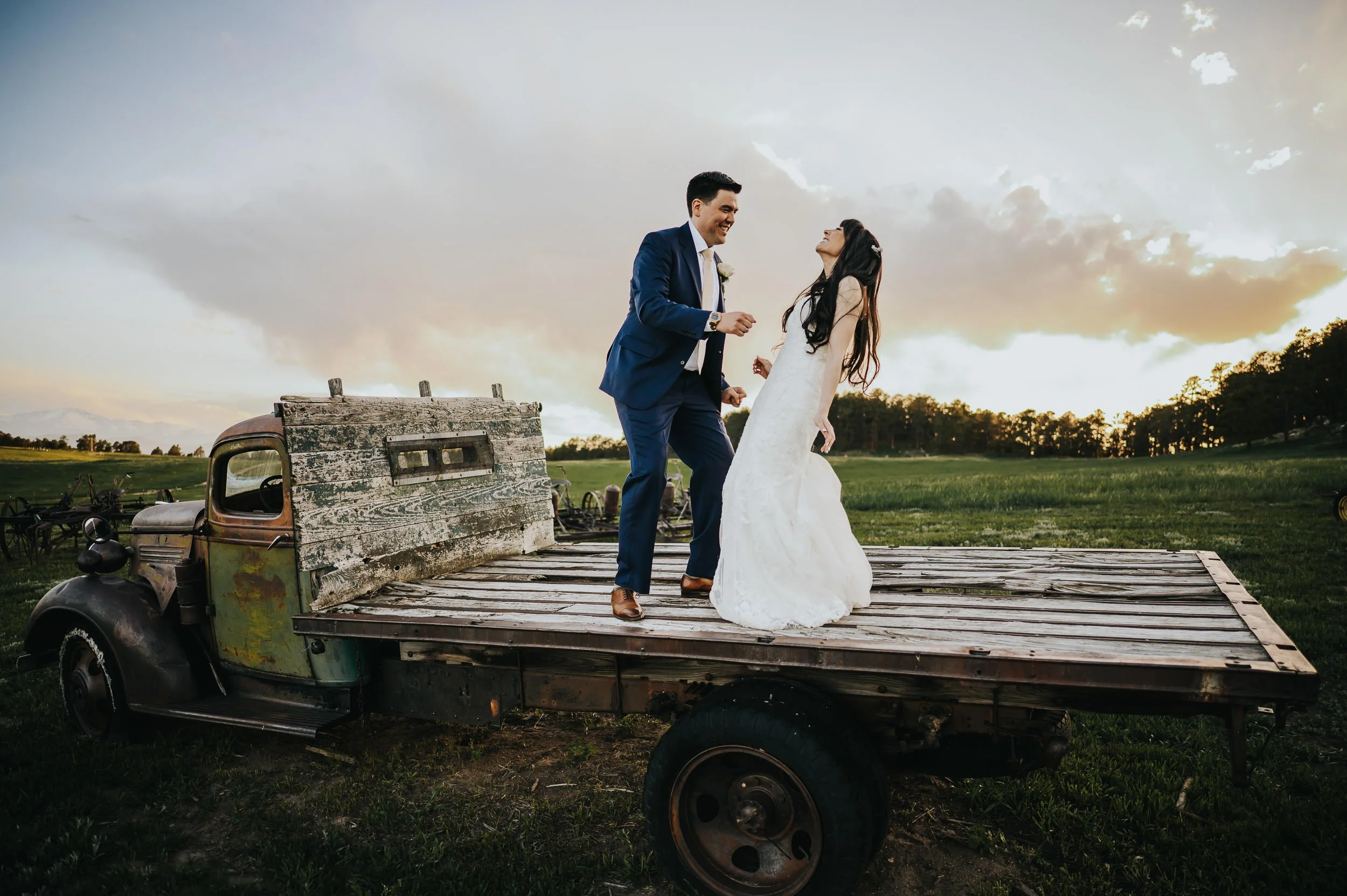 Bride and groom laughing together on a wooden platform at Younger Ranch in Colorado Springs with red rocks in the background.