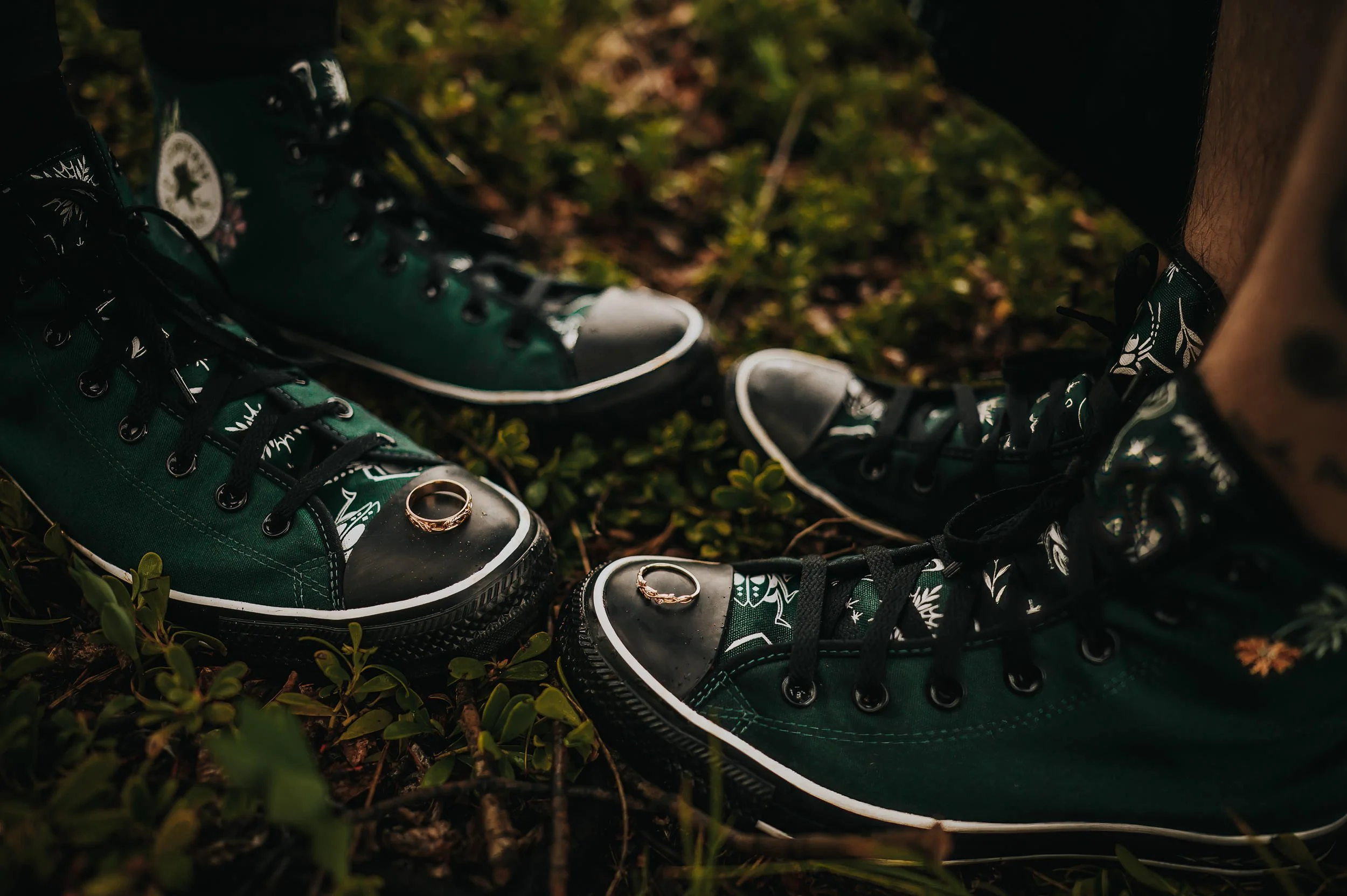 Close detail of green Converse sneakers with wedding rings resting on top.