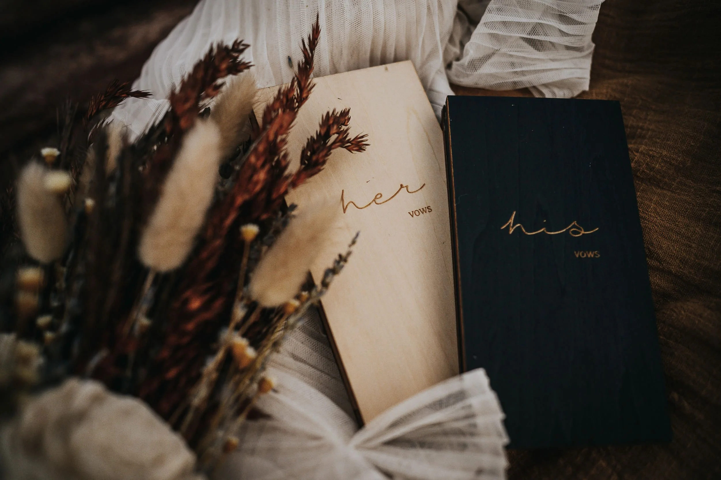 A wedding flatlay with two vow books, dried florals, and pampas grass arranged on a neutral surface.