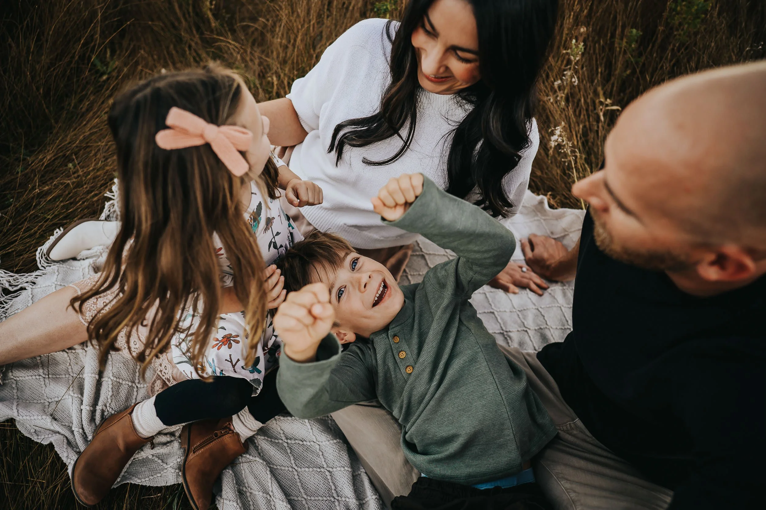 Children snuggle their parents while sitting on a blanket and holding each other tight in the tall grass at Ute Valley Park.