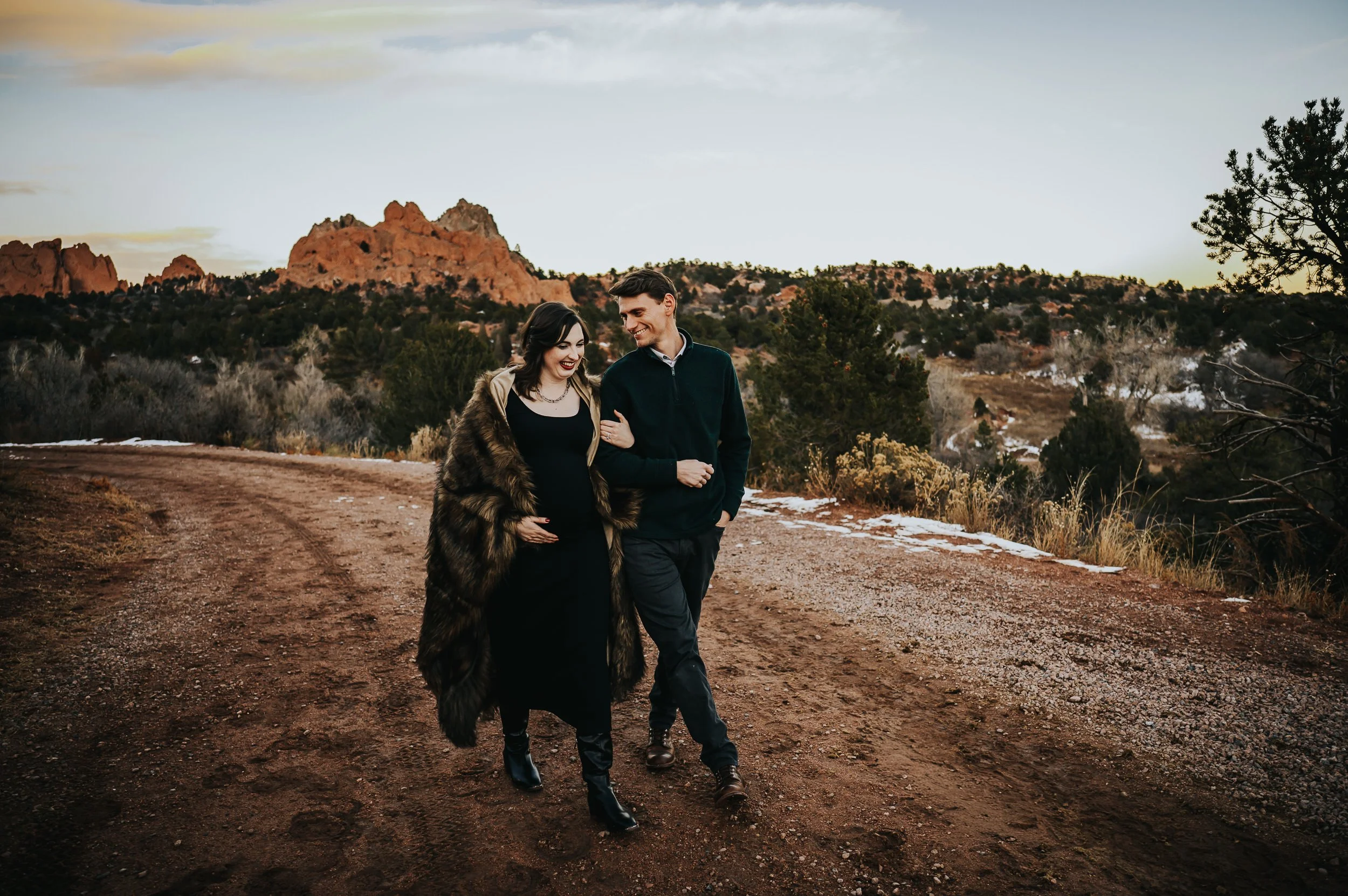 Expecting couple embracing during maternity session at Garden of the Gods with red rocks behind them.