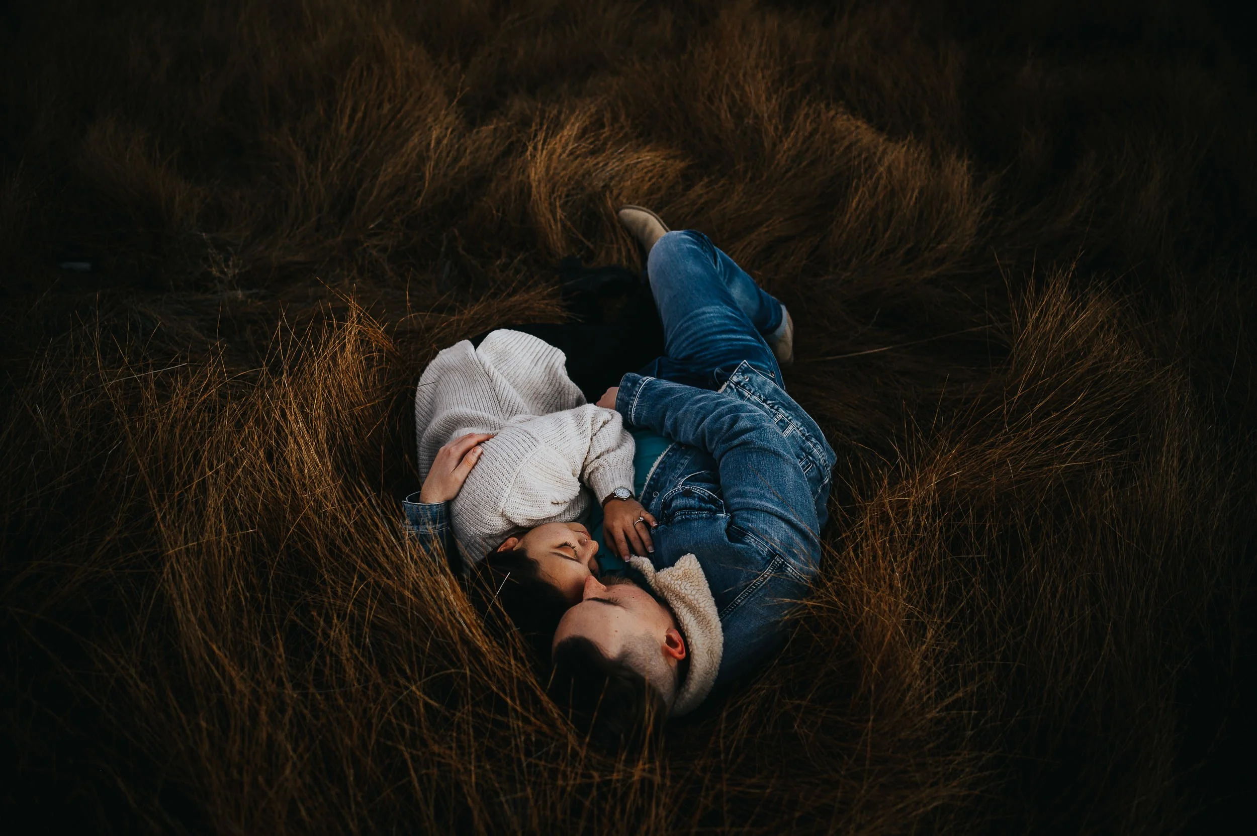 A couple lies together in tall golden grass, overhead portrait, faces close and tender at Lake George, Colorado.