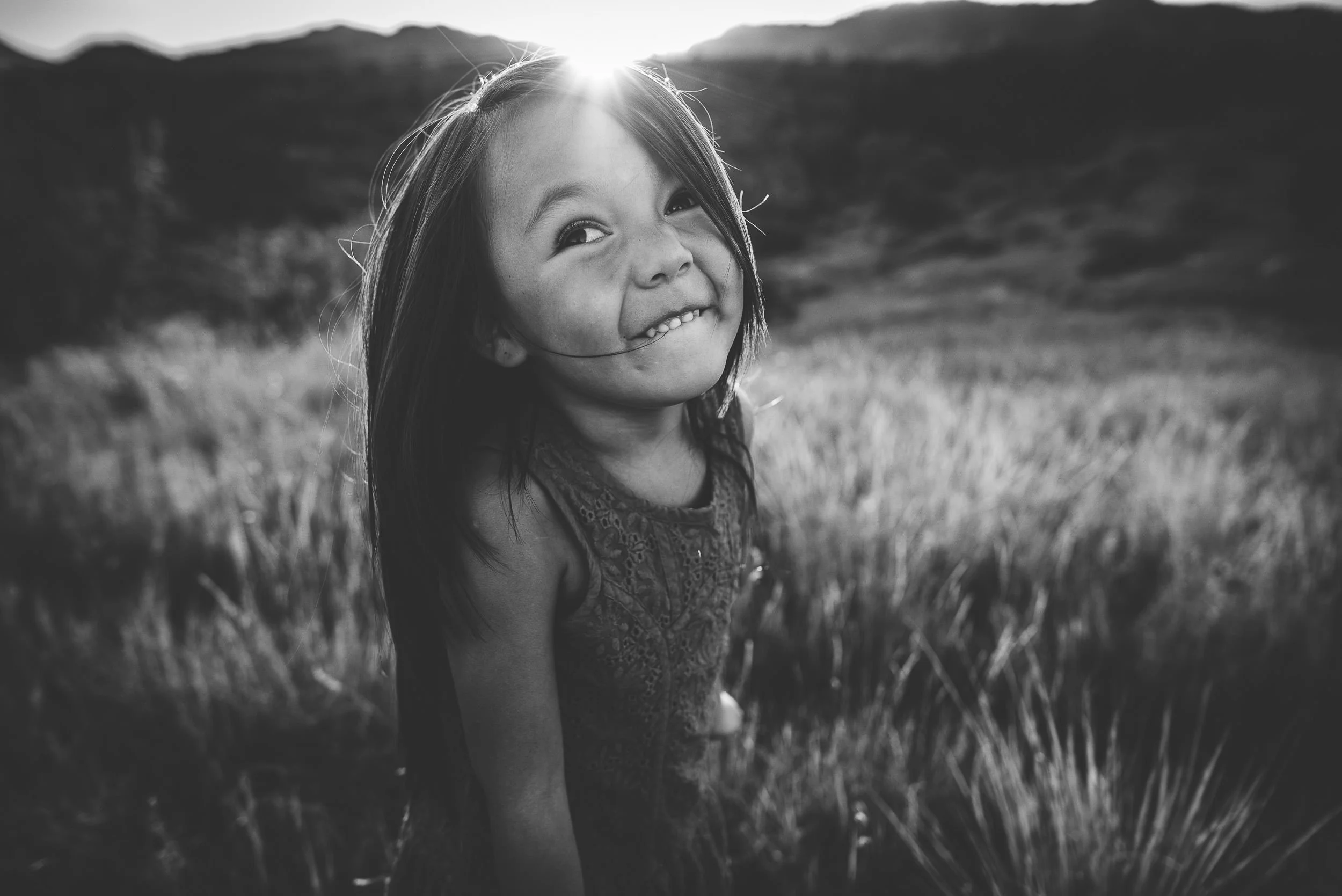 Little girl grins widely in a black and white portrait with a mountain view in Colorado Springs.