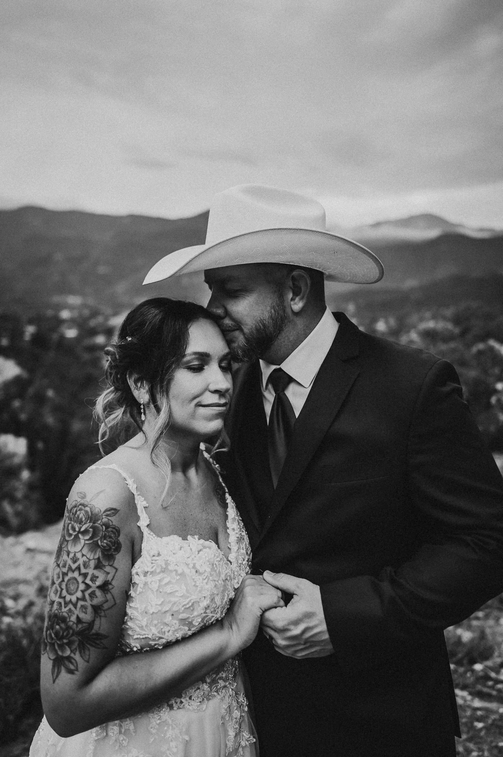 Close black and white portrait of a couple embracing, tattooed arms visible.