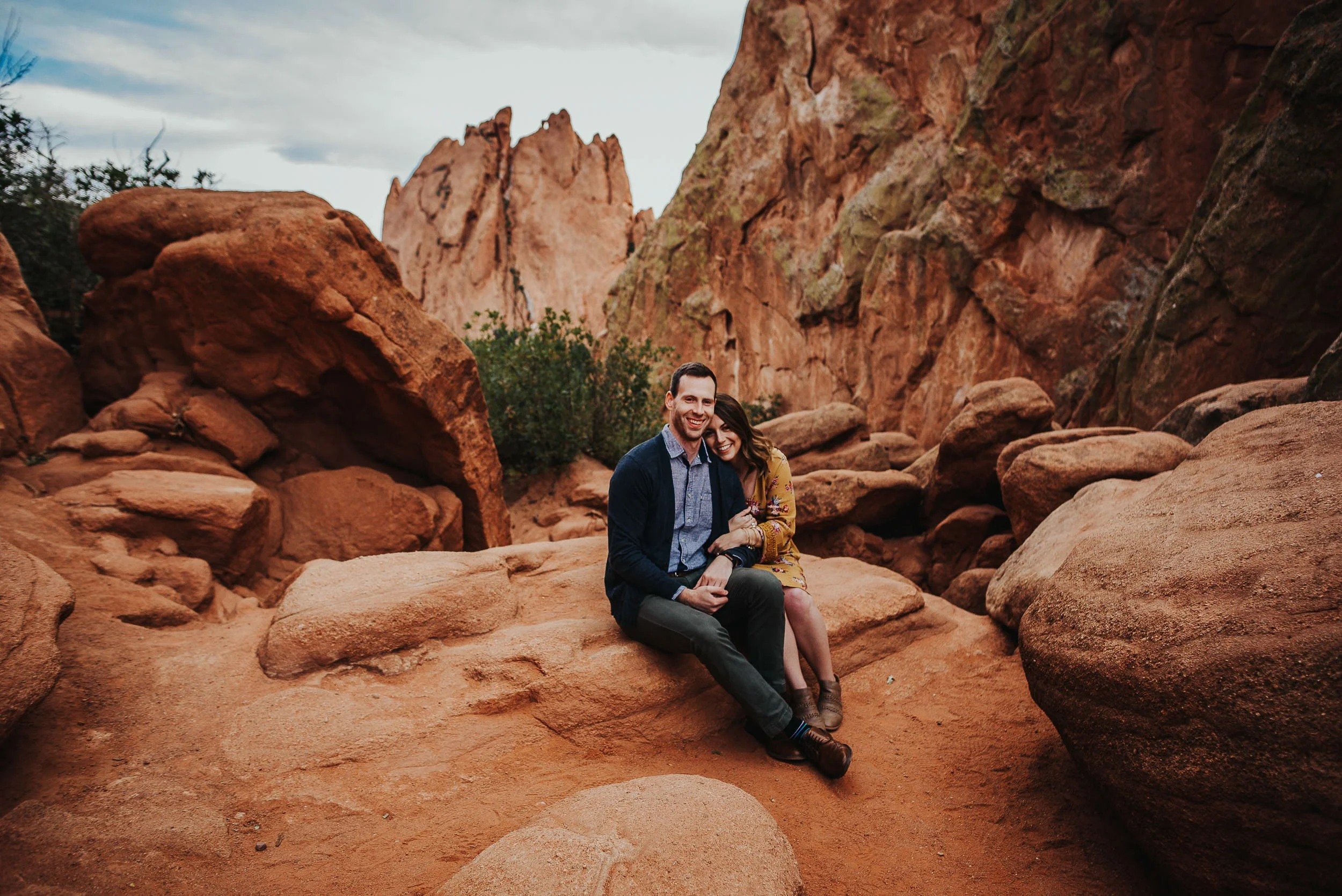 A couple sits close and laughing on red rocks at Garden of the Gods.