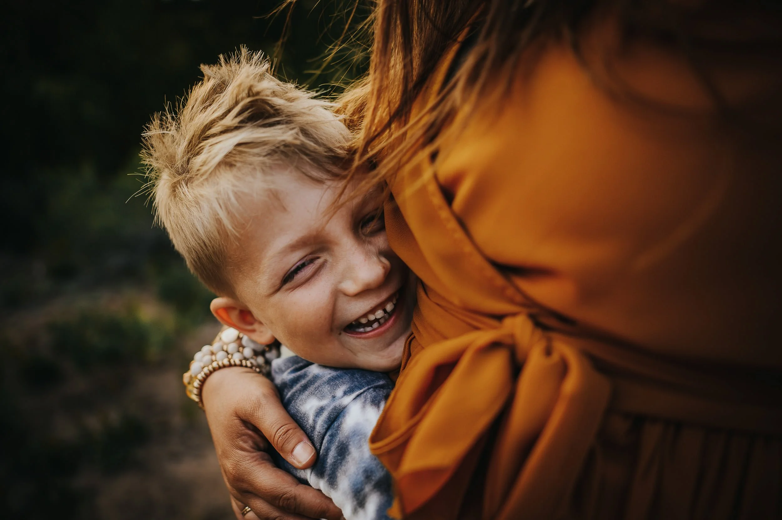 Young boy grins widely as he holds onto his mothers waist during a family photo session in Frisco, Colorado.