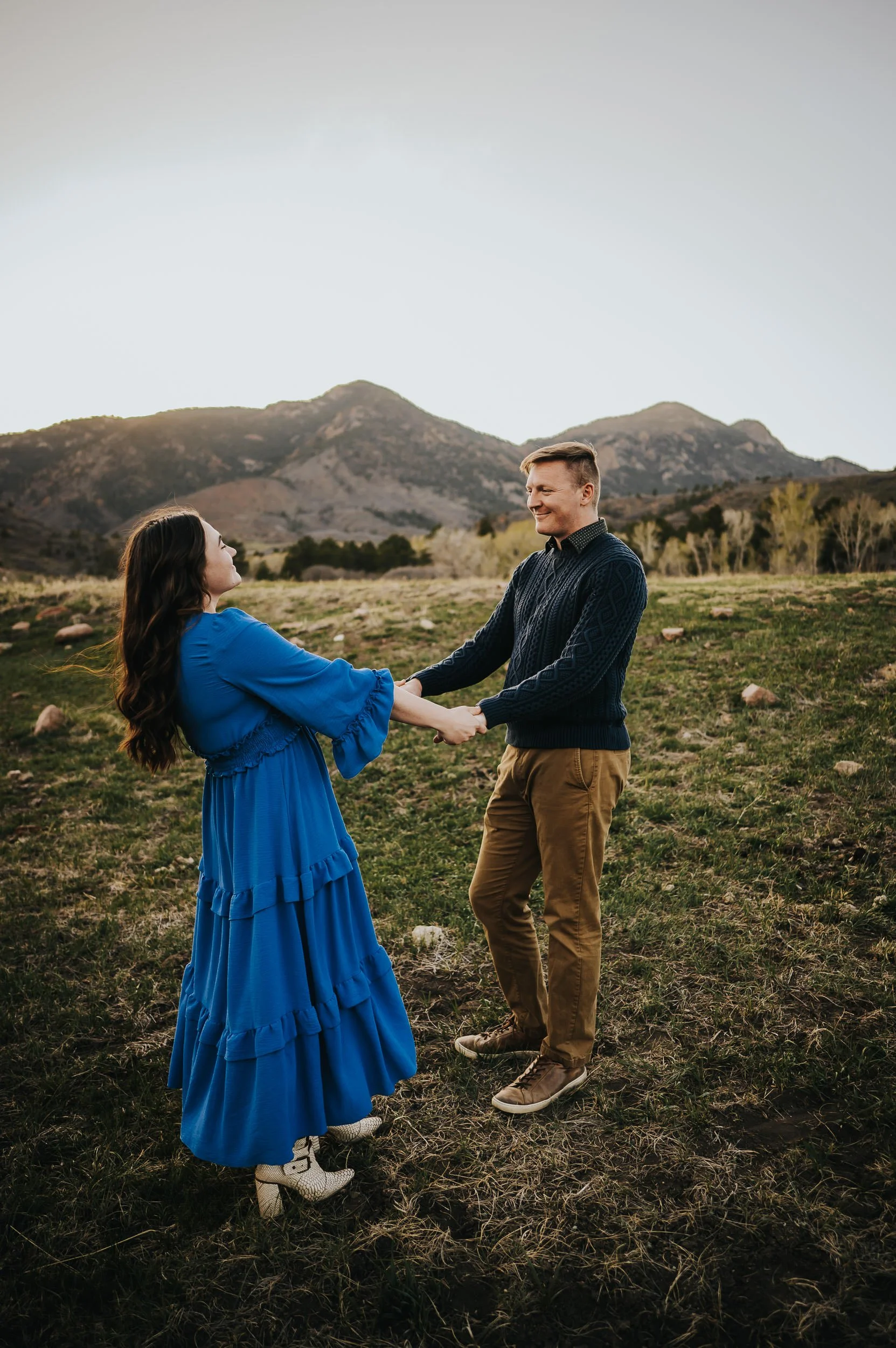 Couple twirling during family session, mom in flowing navy dress catching the wind, rocky Colorado terrain behind them.