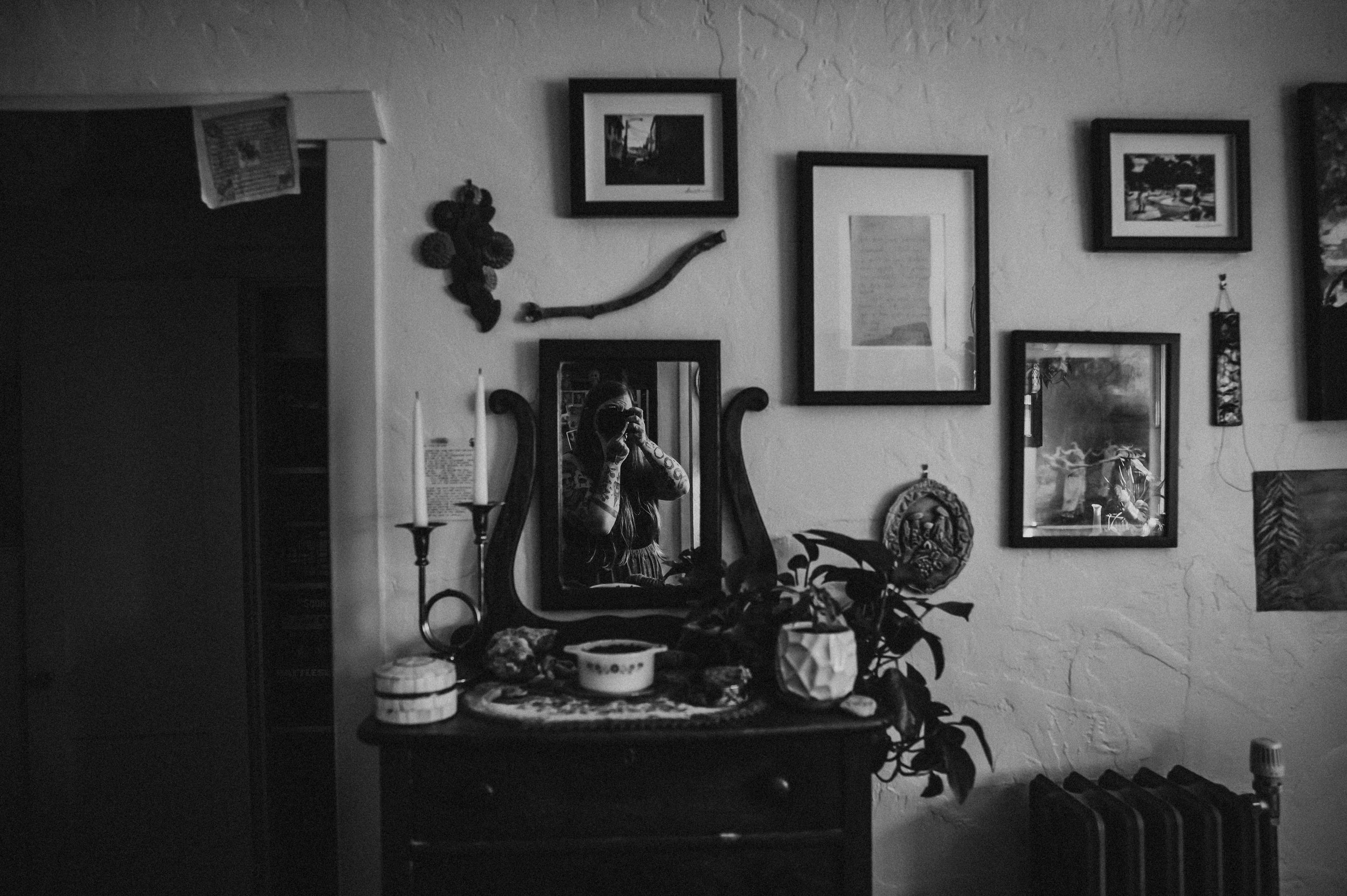 Black and white photo of a wall lined with vintage frames, artwork, and decorative objects.