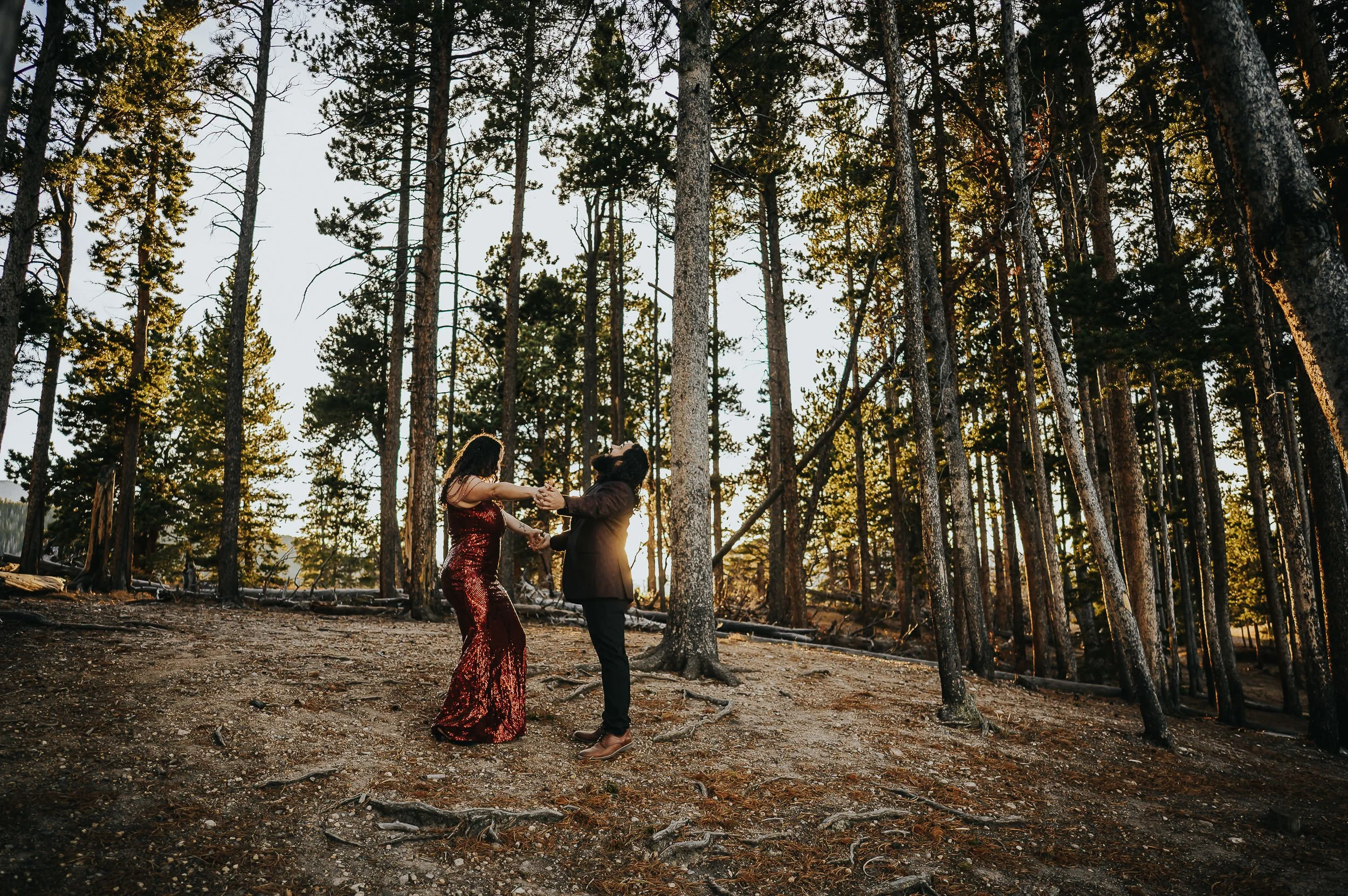 A couple dances together in a golden Colorado forest at sunset, tall pines surrounding them after their proposal session at Sprague Lake in Rocky Mountain National Park.