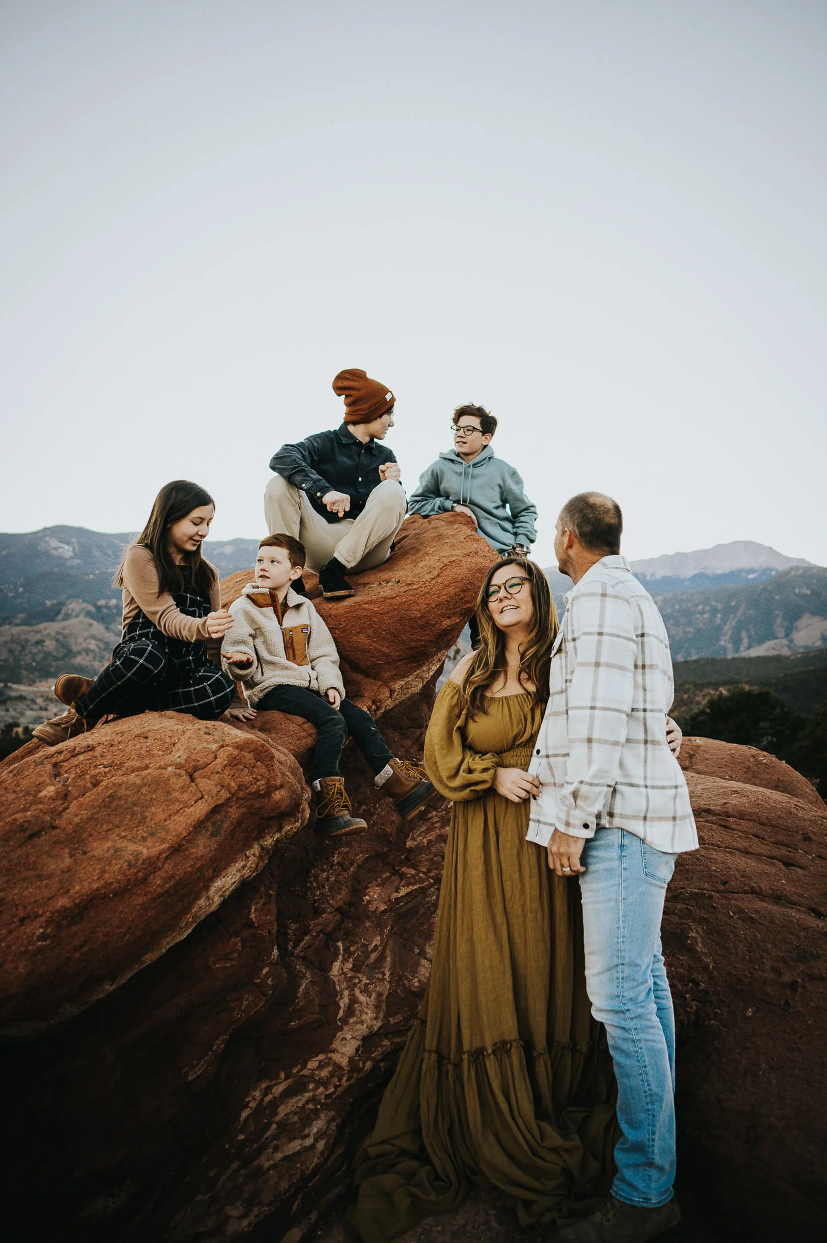 Extended family with teens sitting on red rock formation in coordinated cool tones including navy, teal, mustard, and cream