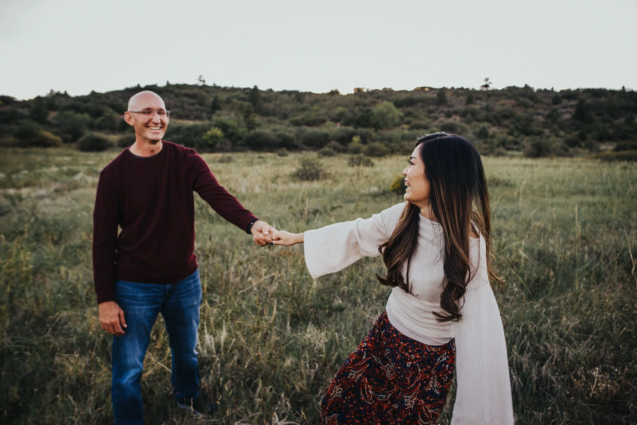 A couple walks hand in hand through a wide Colorado meadow, smiling at each other at Stratton Open Space in Colorado Springs.