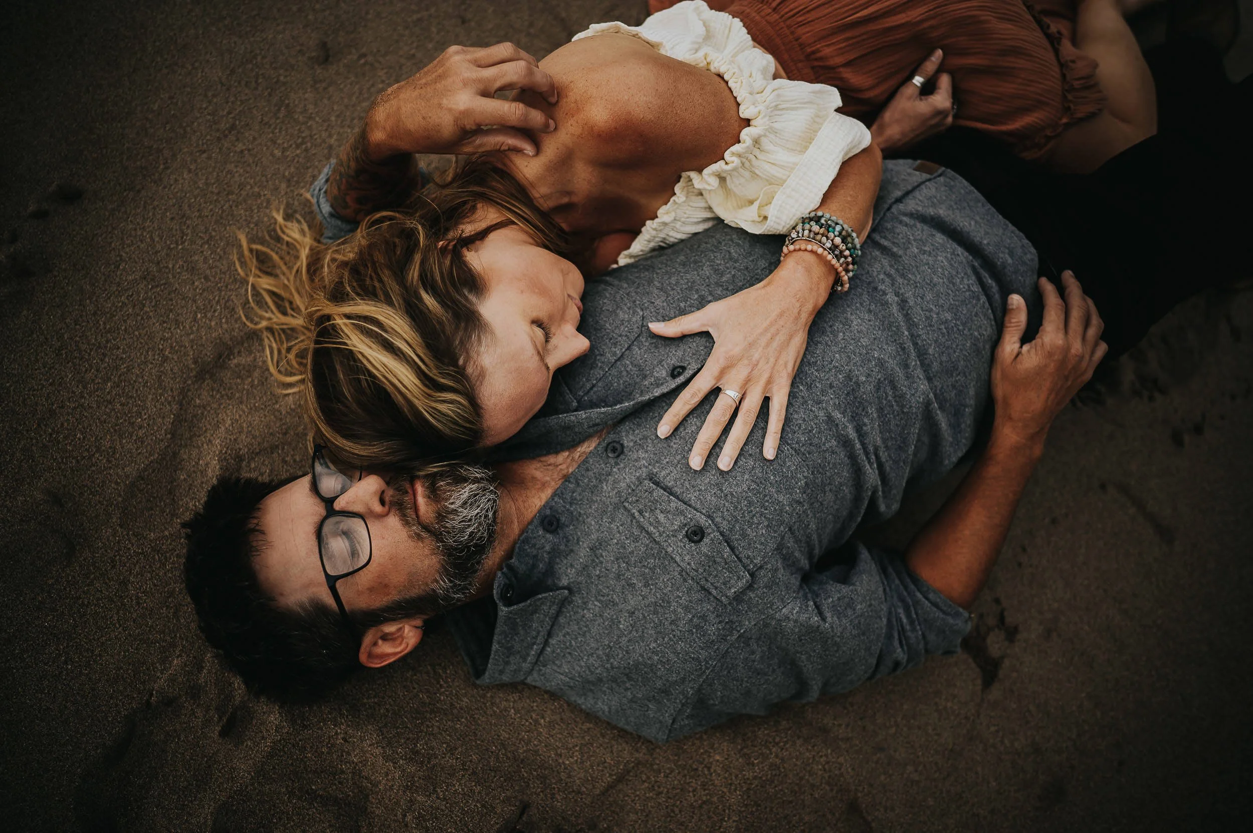 A couple lies in the grass together, faces upside down and close, laughing and relaxed.