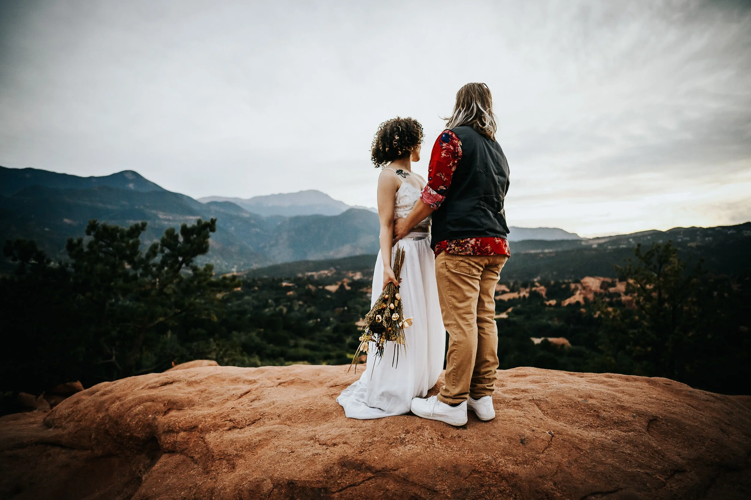 A bride and groom stand together from behind, overlooking a Colorado mountain landscape.