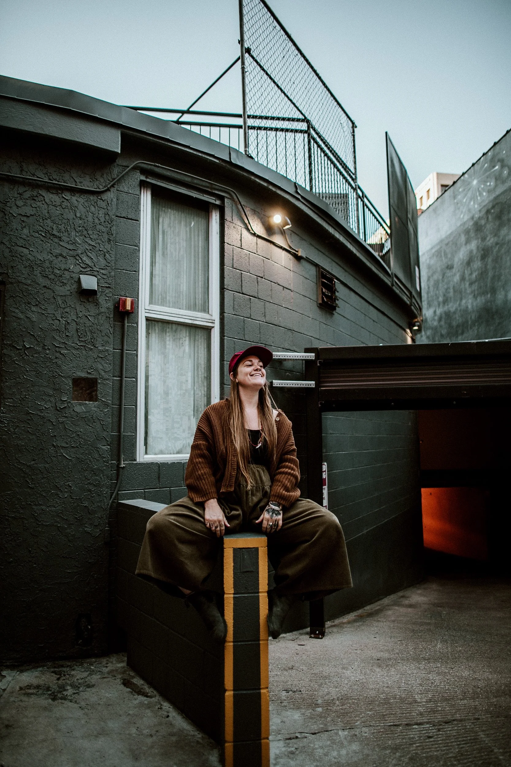 Sandy, Colorado Springs photographer, sitting on outdoor steps beside a warmly lit building at night.