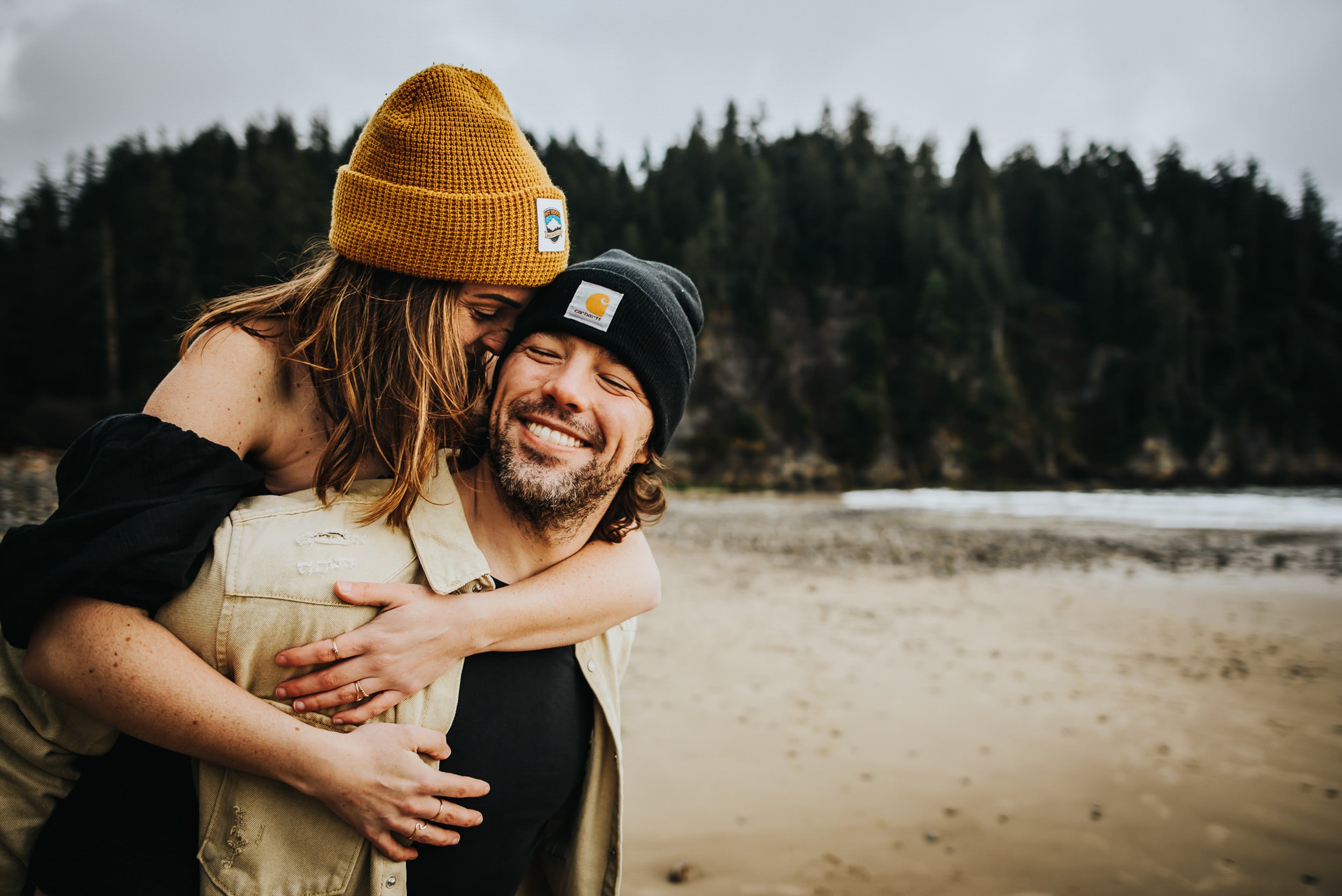A man in a knit hat laughs and holds his partner close in a Colorado mountain landscape, full of warmth.