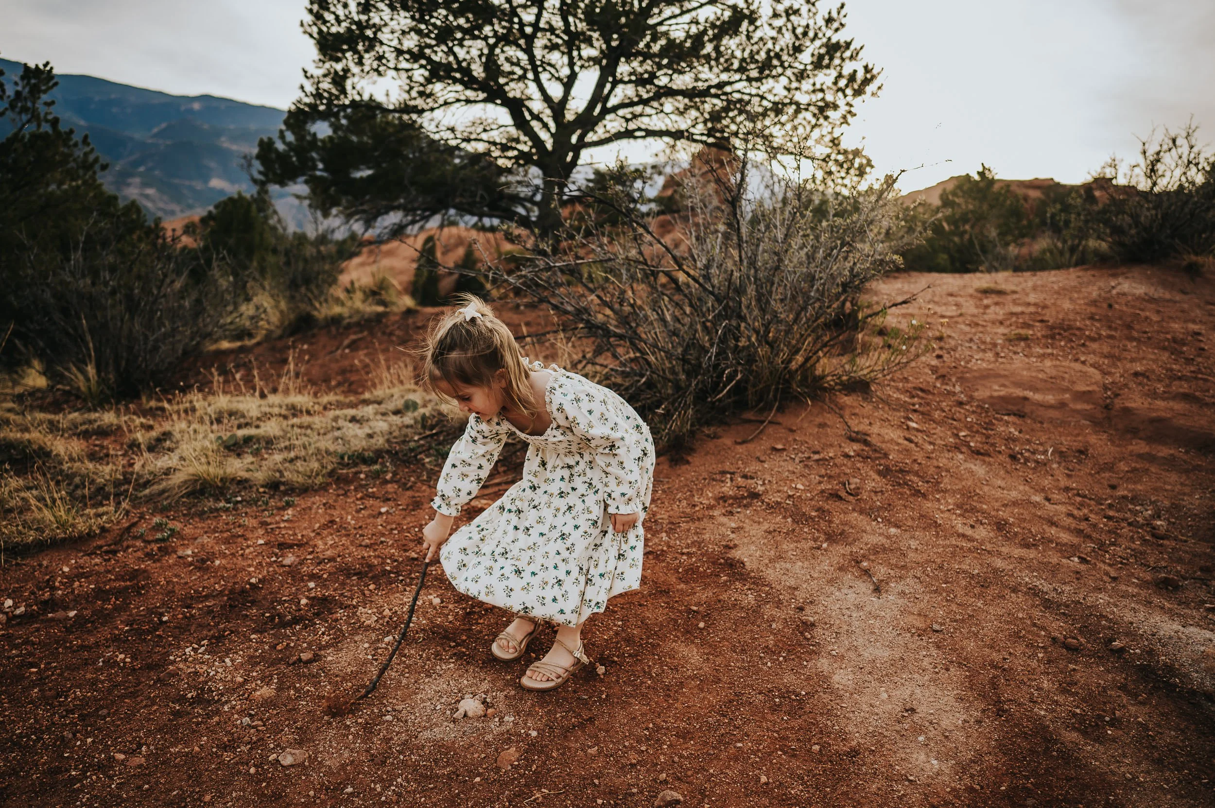 Little girl in a white floral dress twirling while her mom watches.