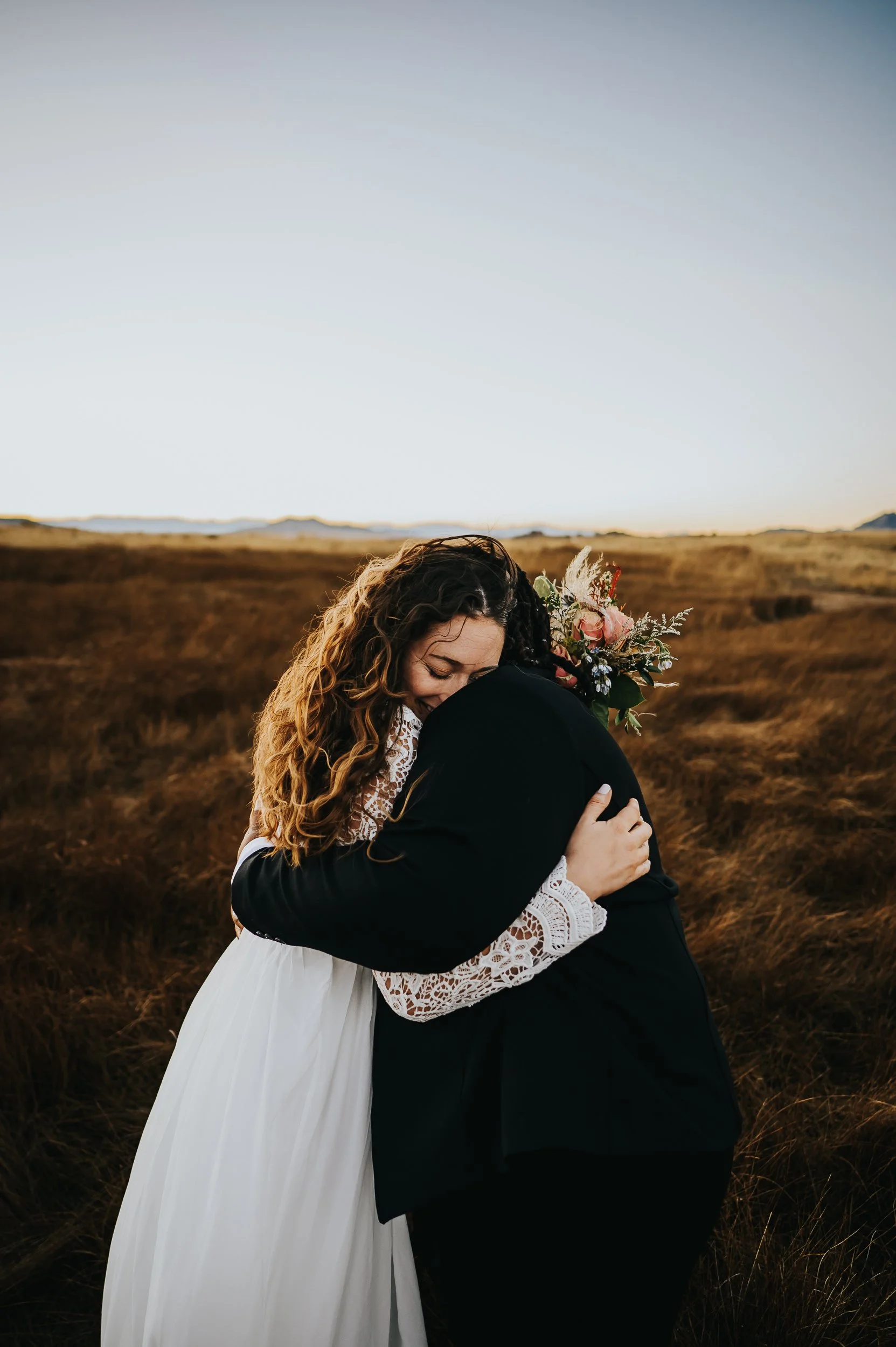 Two brides walking through a meadow at sunset after their elopement ceremony.