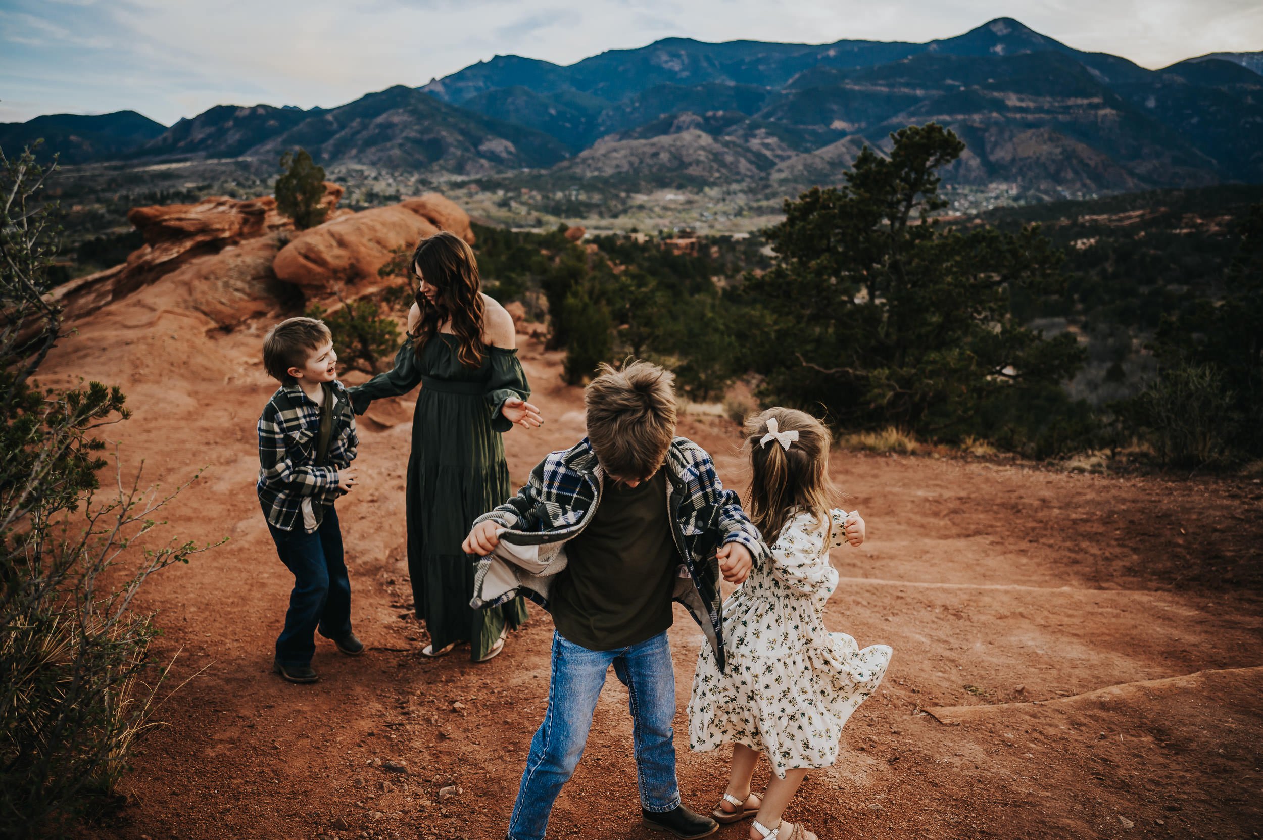 Three siblings holding hands in a circle on a dirt path, mountains behind.