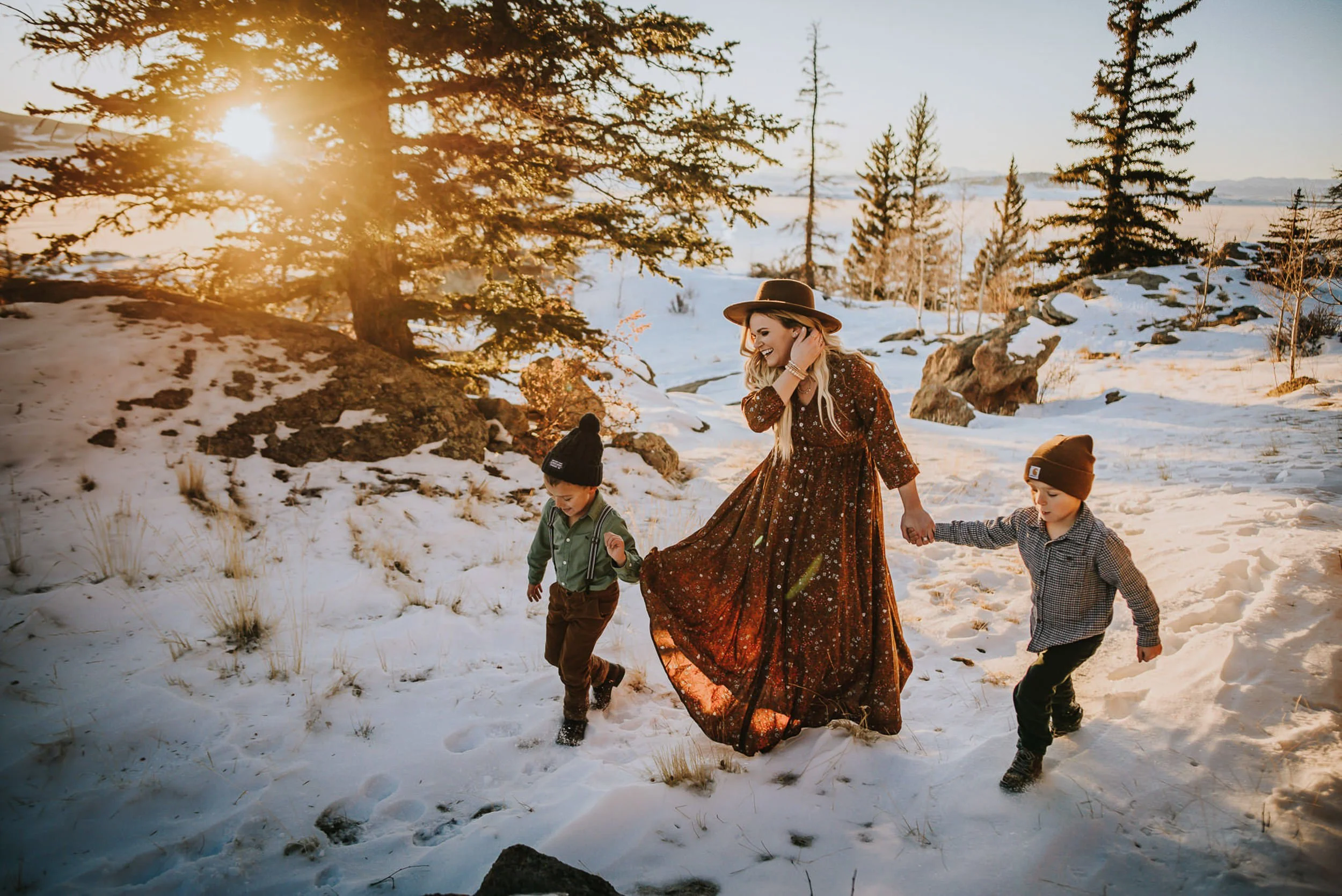 Family of three running through the snow while the sun shines through the trees and blankets them in golden light.